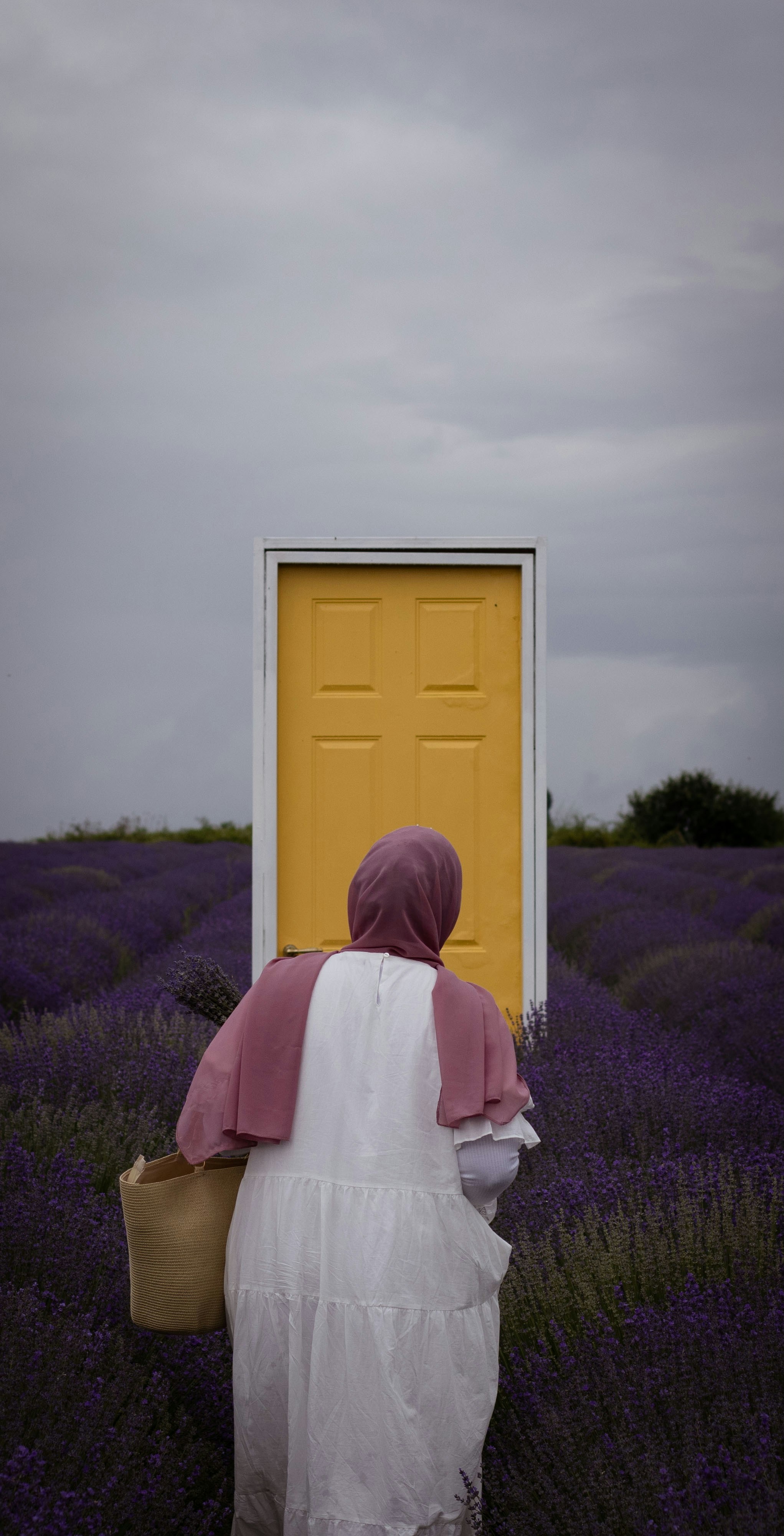 A woman approaches a yellow door in a lavender field.