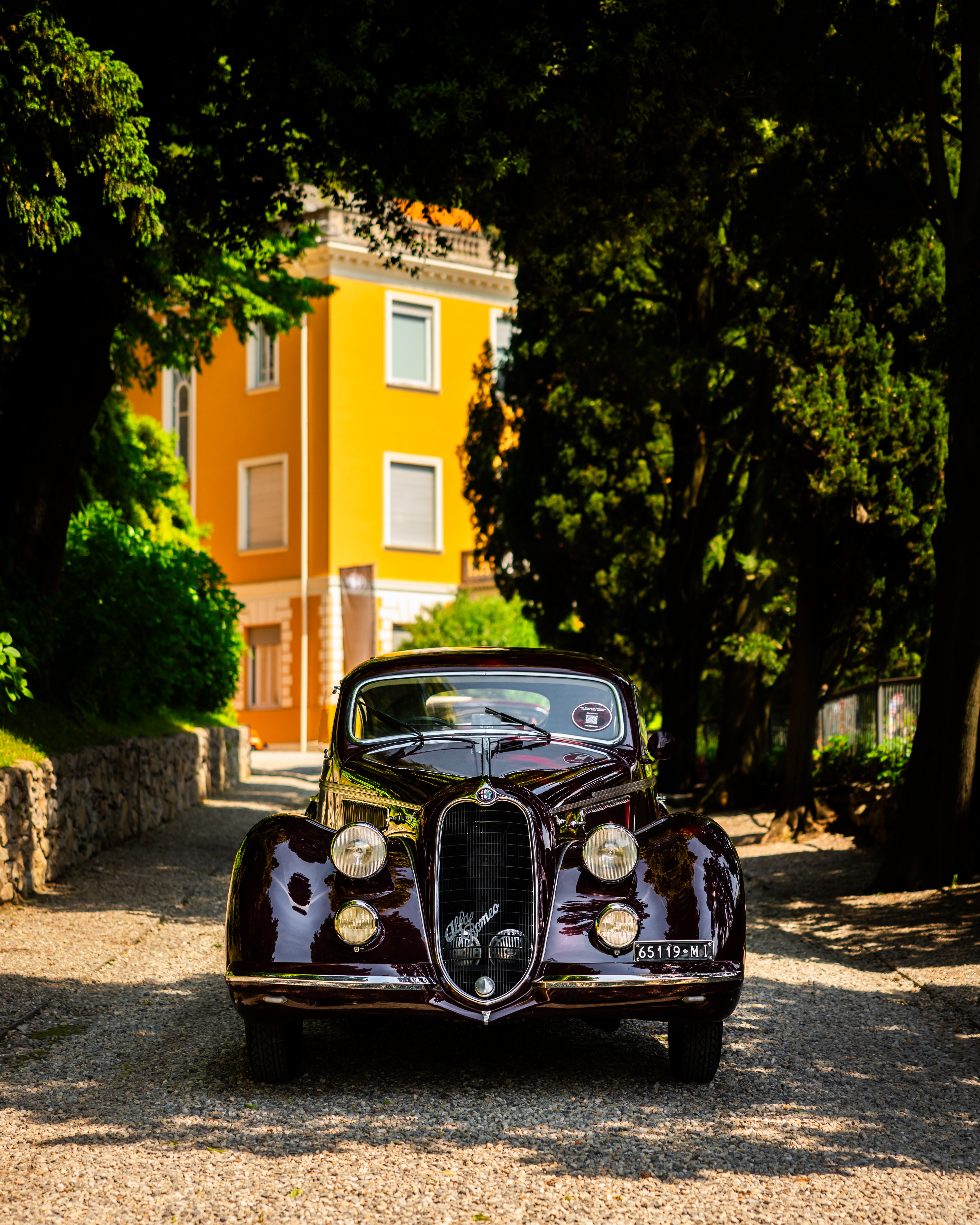 A vintage car parks in front of a yellow building.