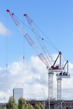 Two tower cranes stand in front of a blue sky.