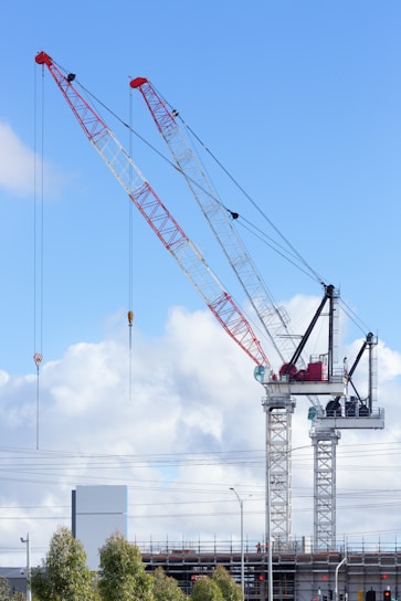 Two tower cranes stand in front of a blue sky.