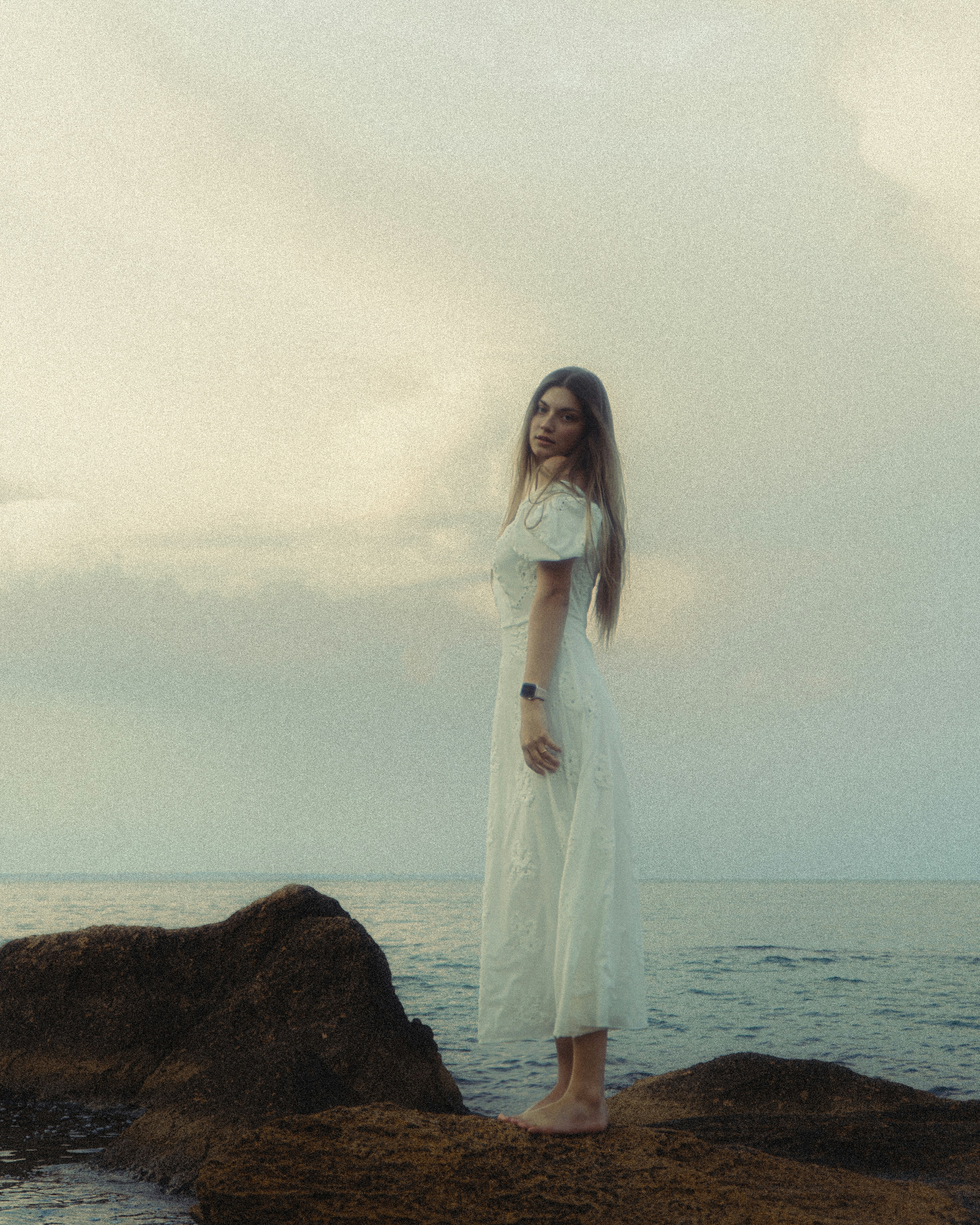Woman stands on a rock near the sea.