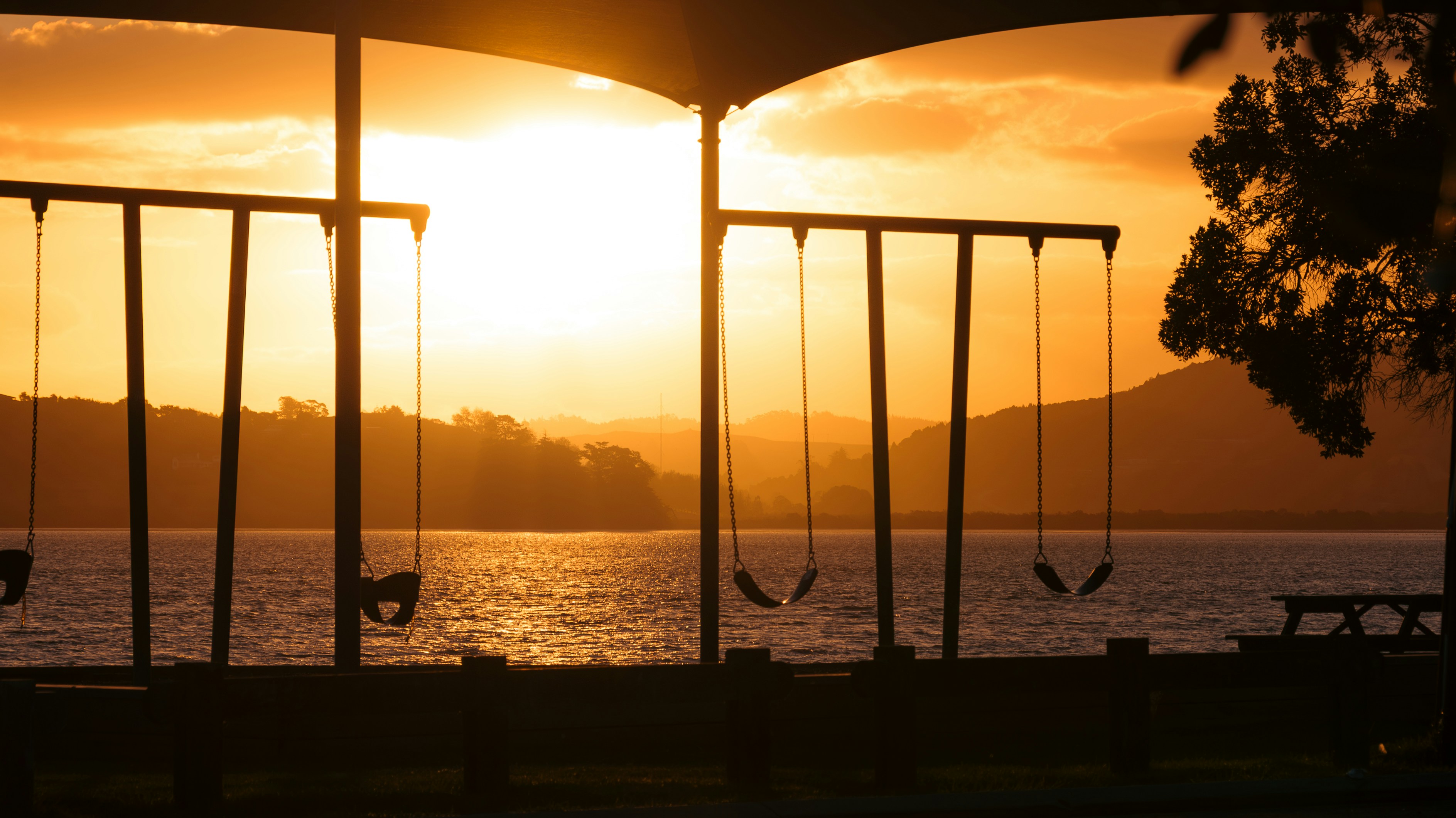 Golden sunset over lake with swings.