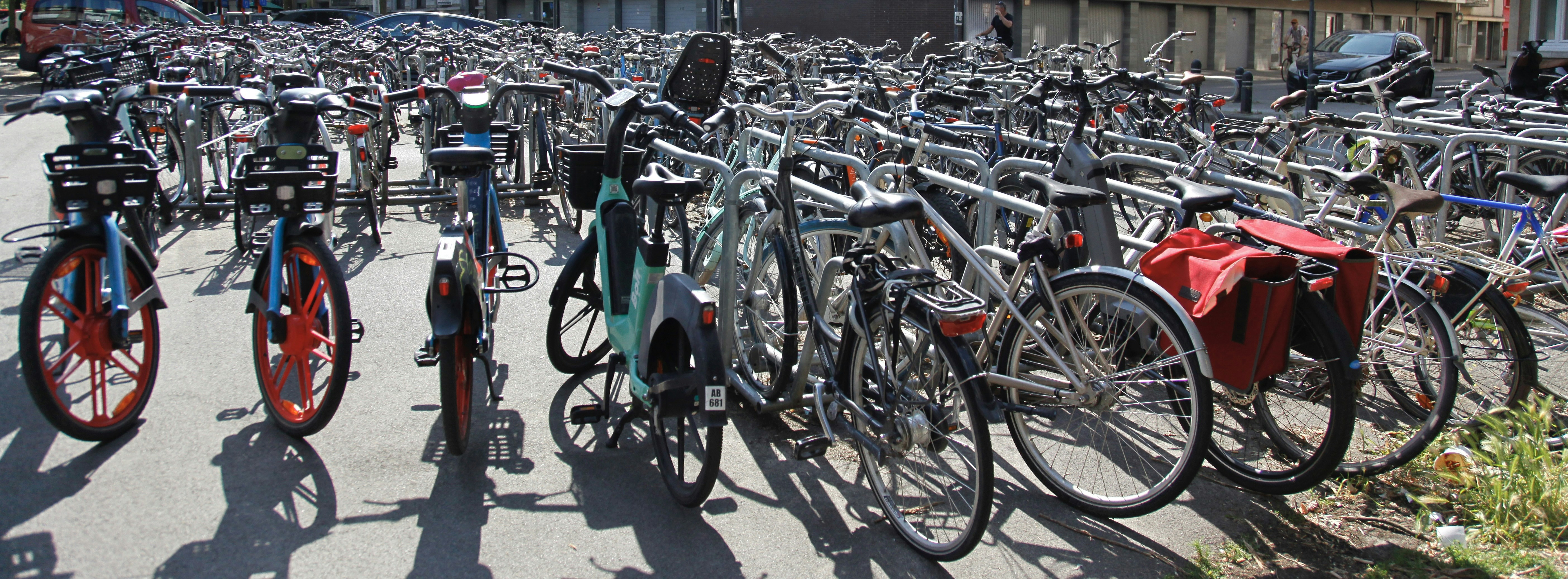 Bikes are parked in a very crowded bike rack.