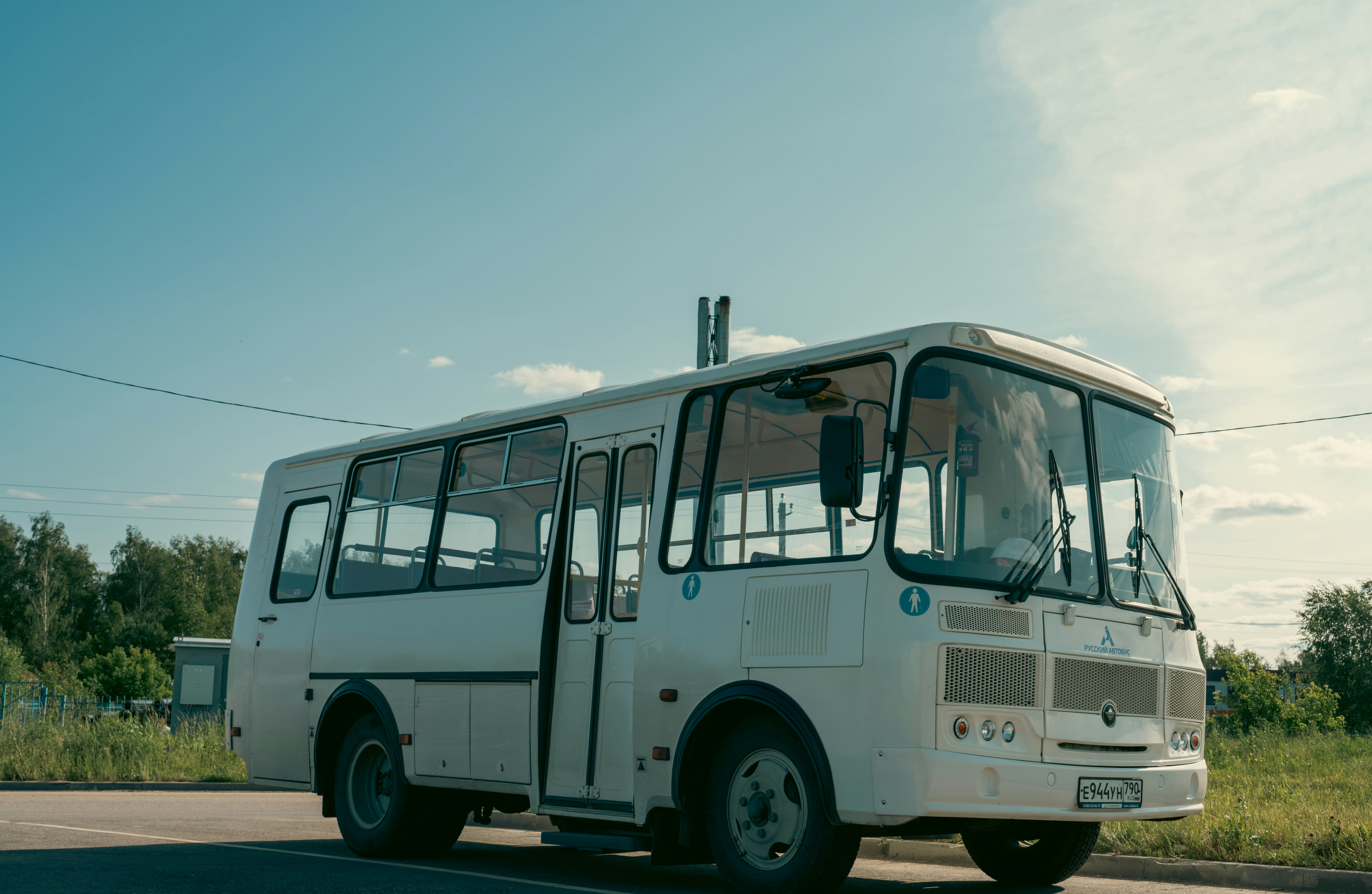 A white bus sits on a road under blue skies.
