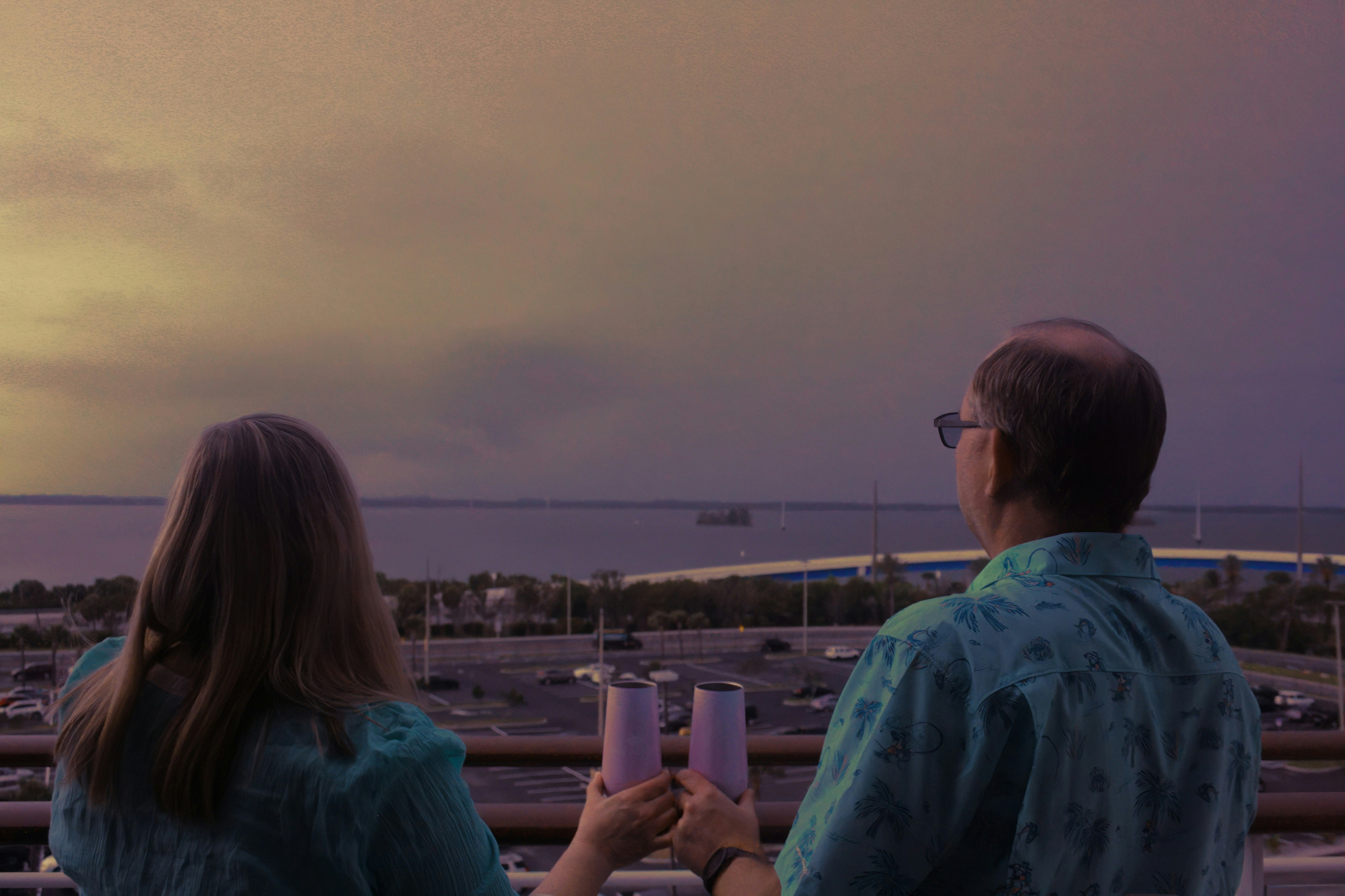 Couple celebrates with drinks, overlooking a bridge.