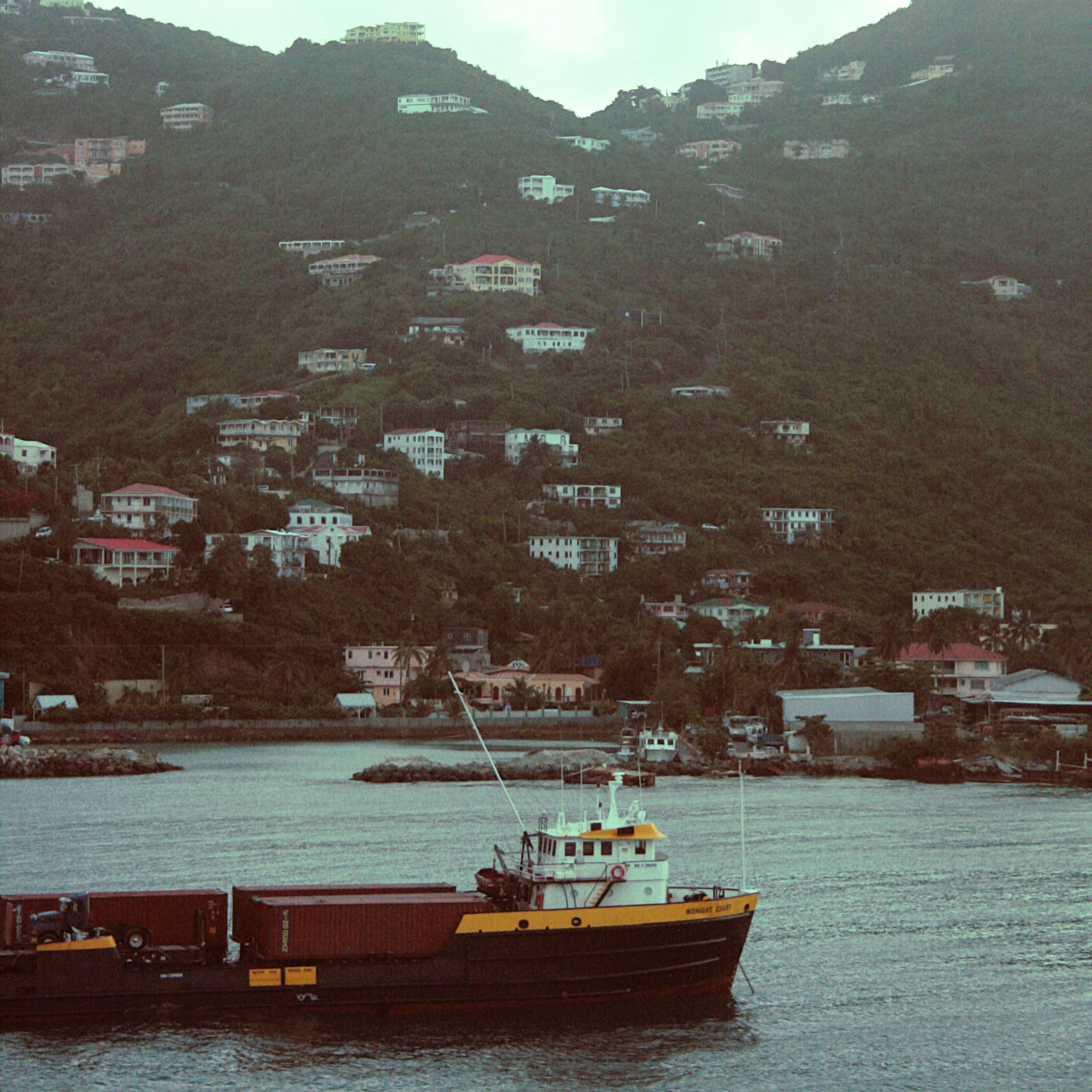 A boat sails in front of a mountainside village