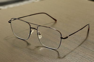 Eyeglasses sit on a light-colored, wooden surface.