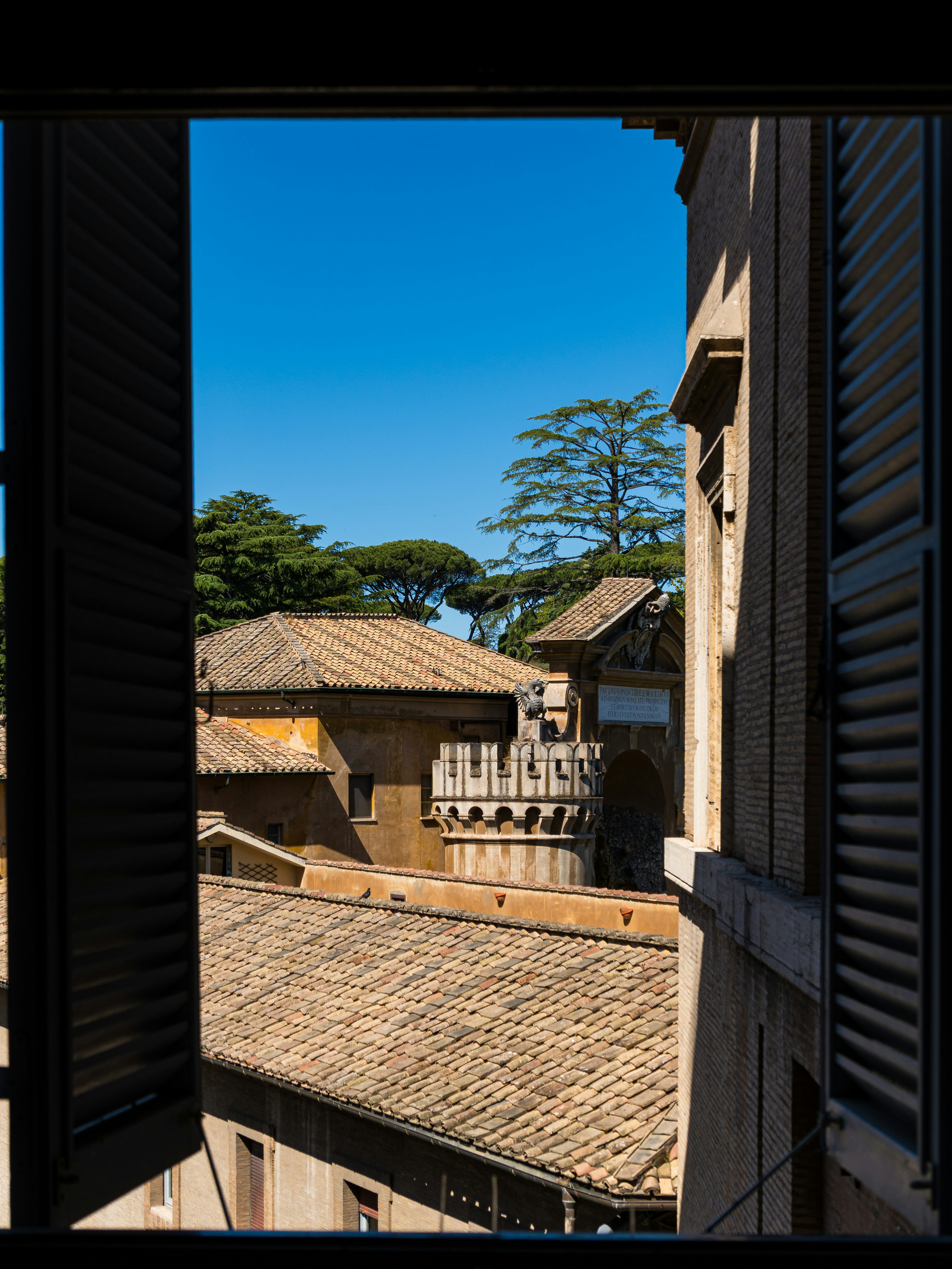Buildings and trees are viewed from an open window.
