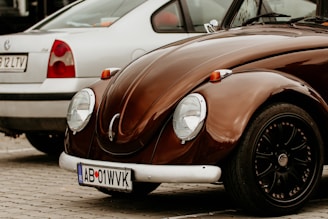 A brown volkswagen beetle next to a silver car.