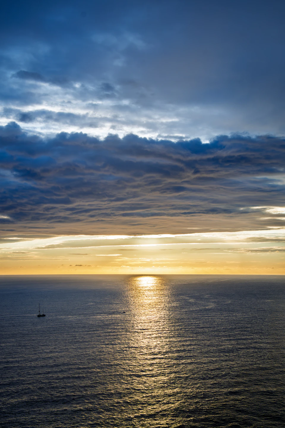 Sunset over the ocean with a small boat sailing across calm blue waters