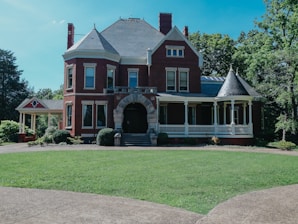 A large, red, victorian house sits in a yard.