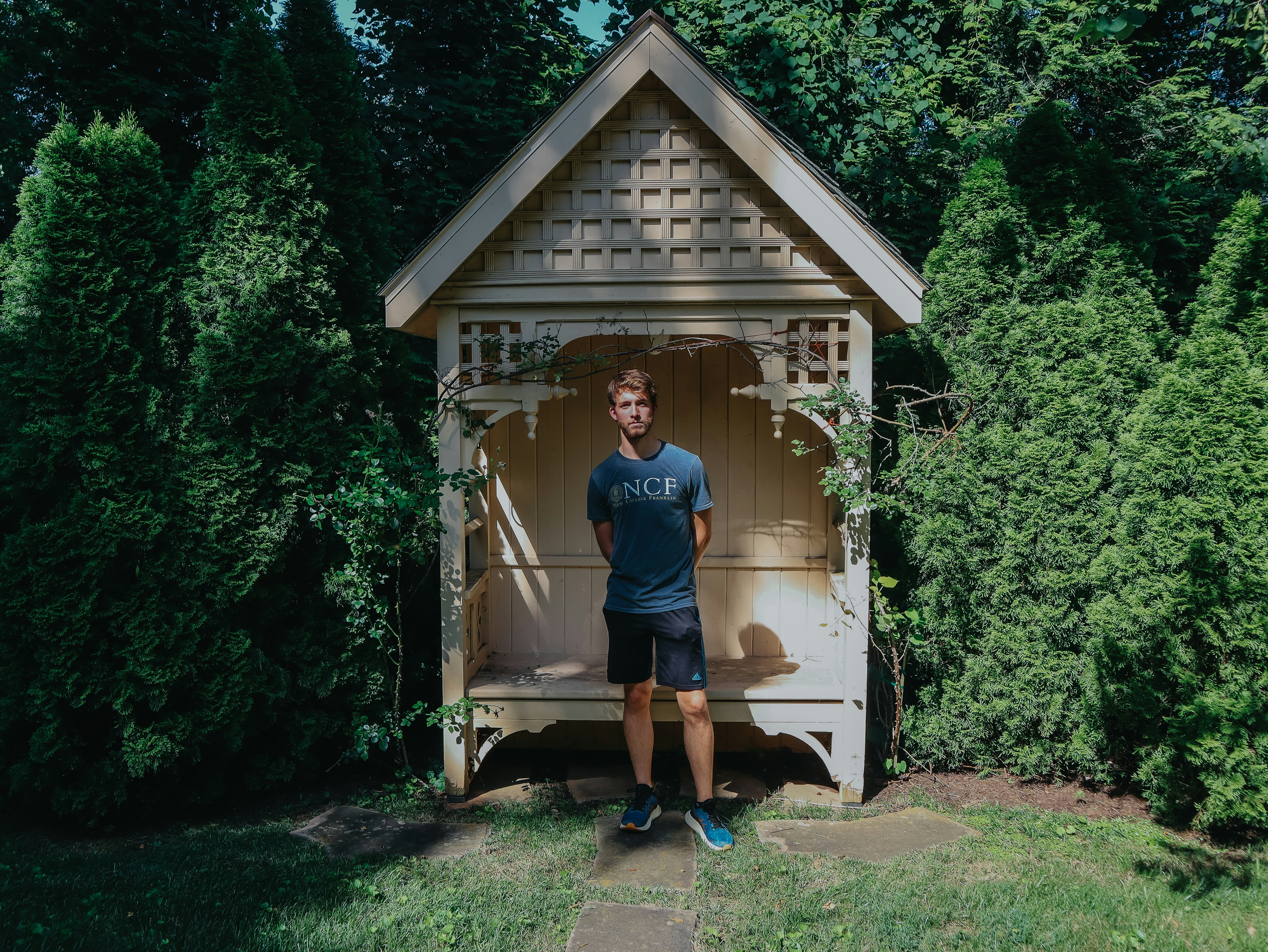A man stands inside a garden arbor.