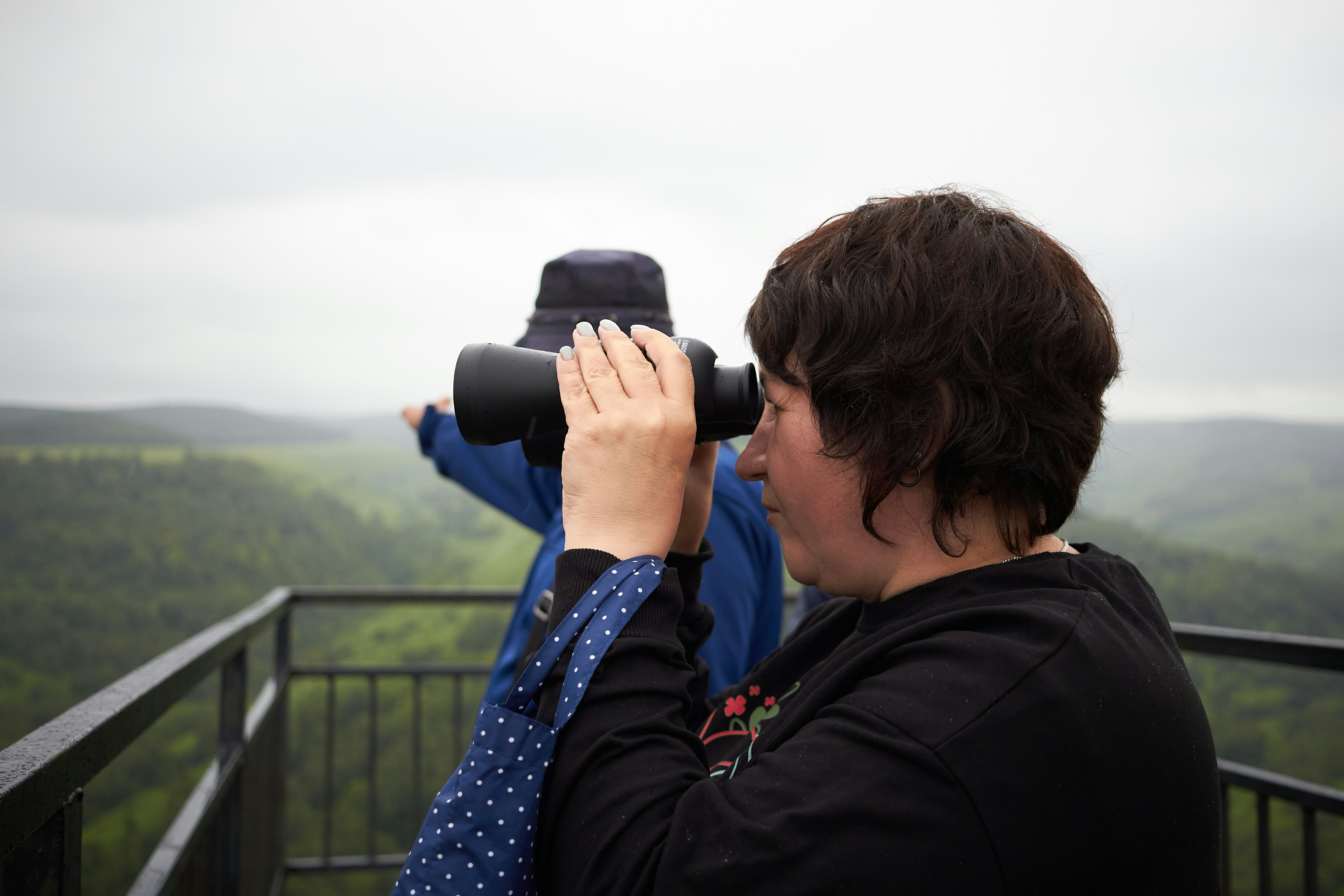 Woman is looking through binoculars at a landscape.
