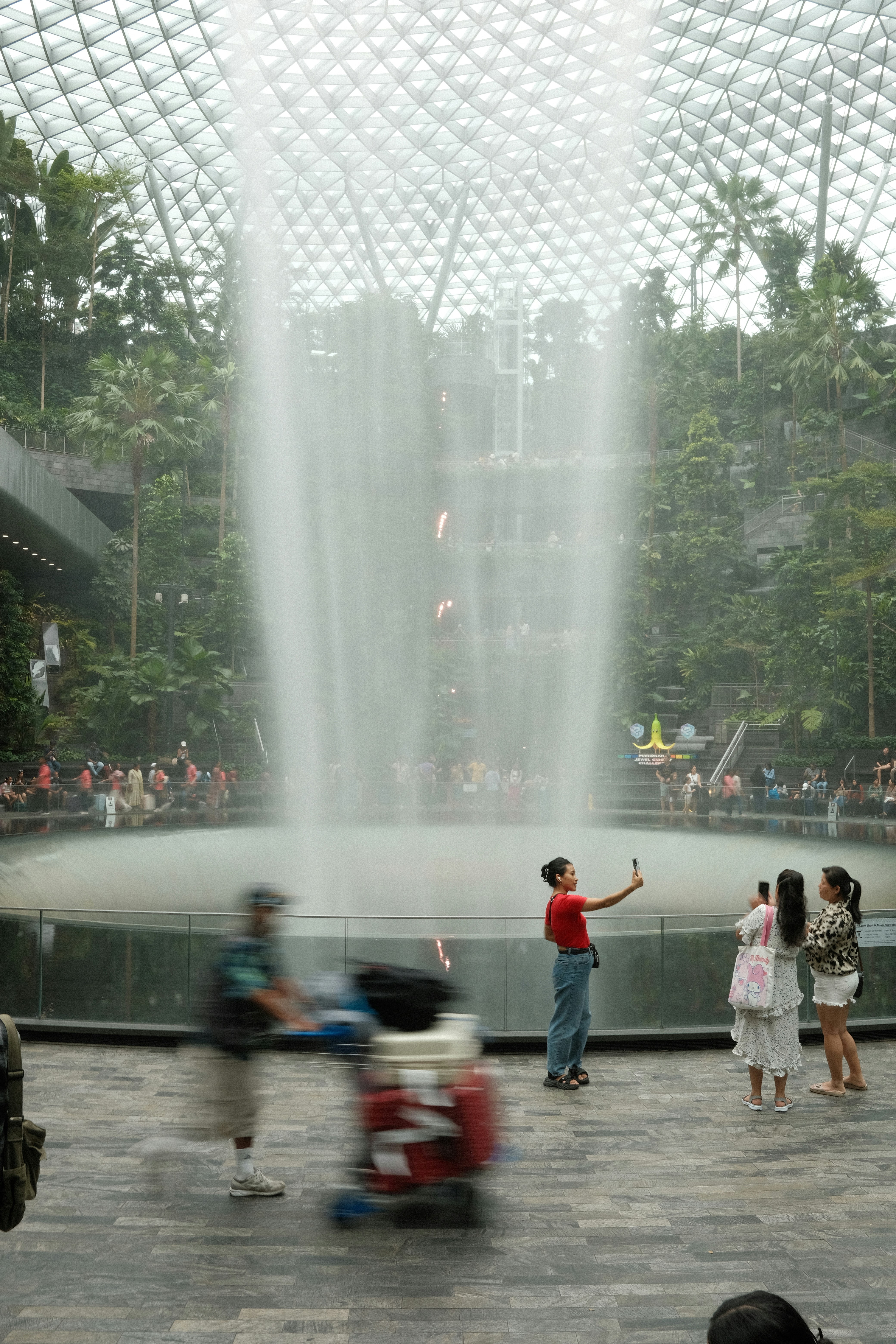 People take photos near a large indoor waterfall.