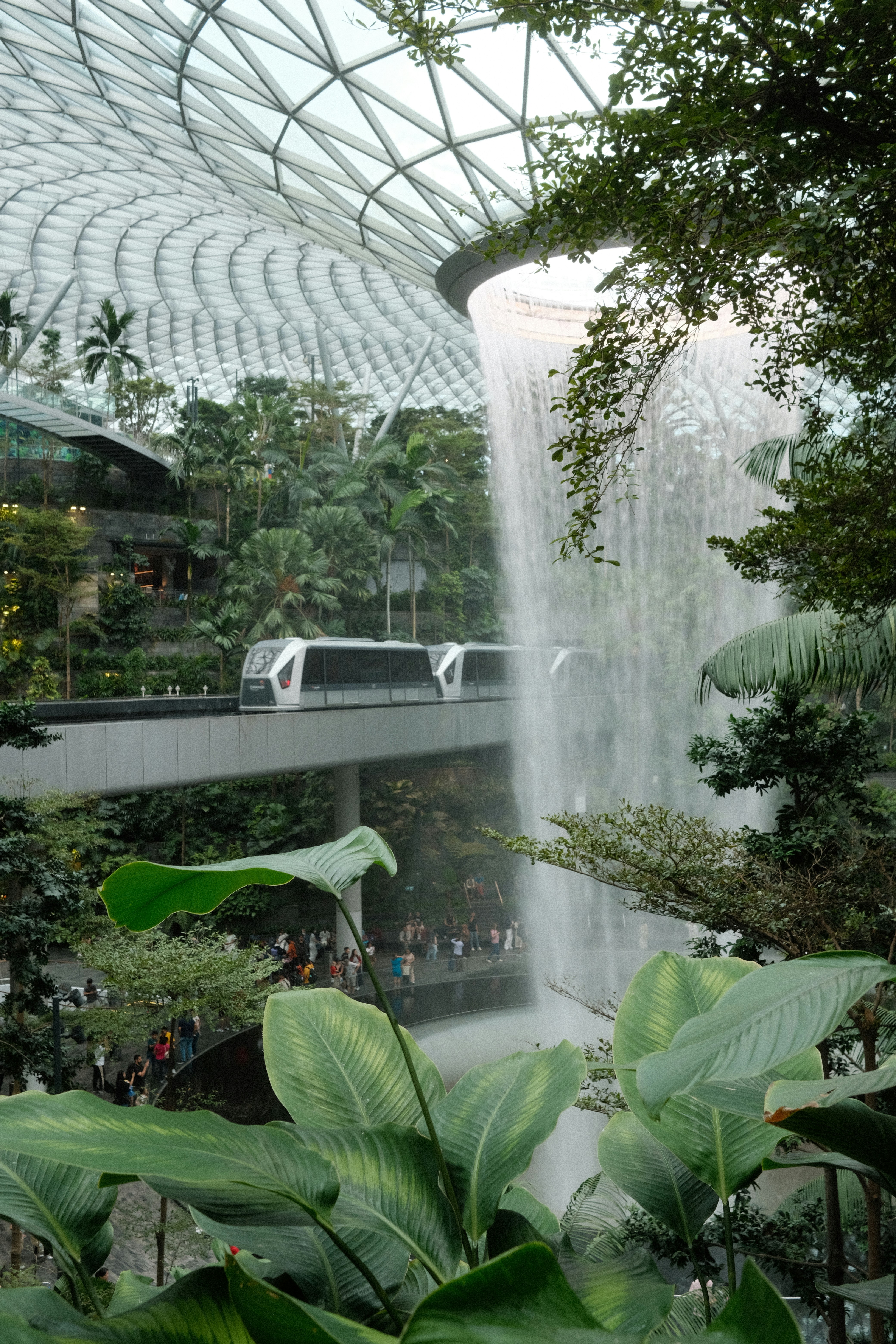 Indoor waterfall with a train and lush greenery.