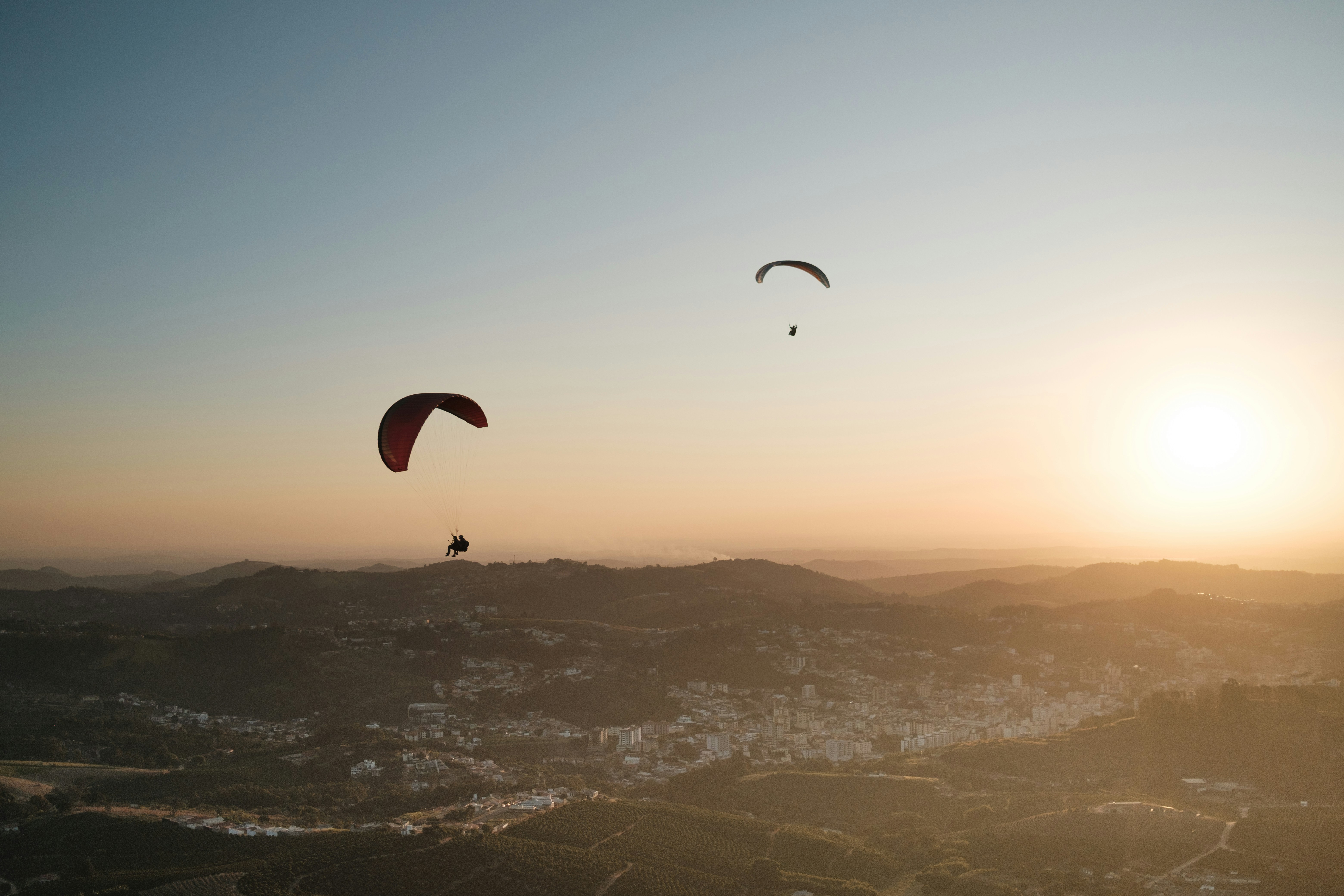 Paragliders float above a hazy sunset landscape.