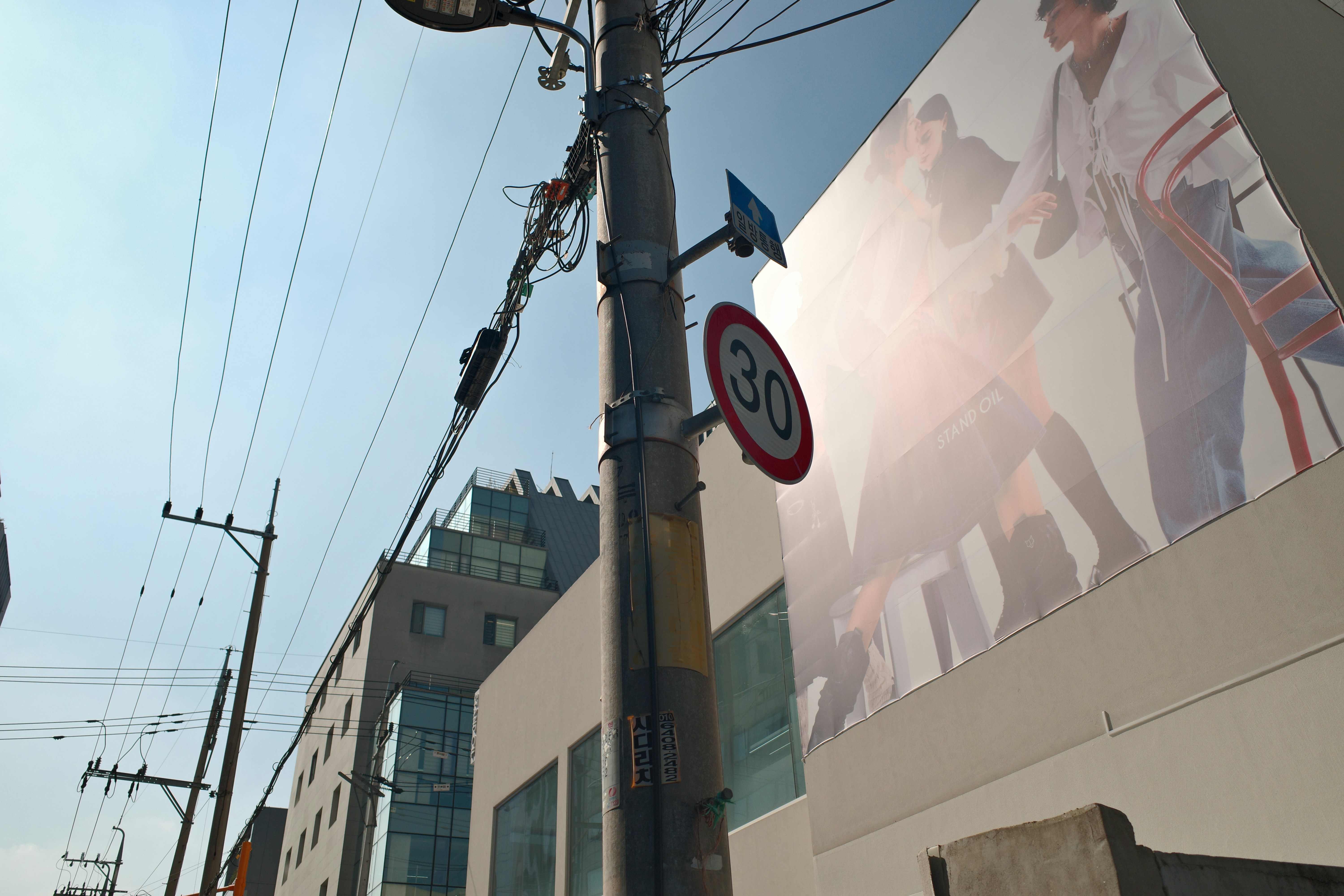 Straßenszene mit Strommast, Schildern und einem Gebäude.