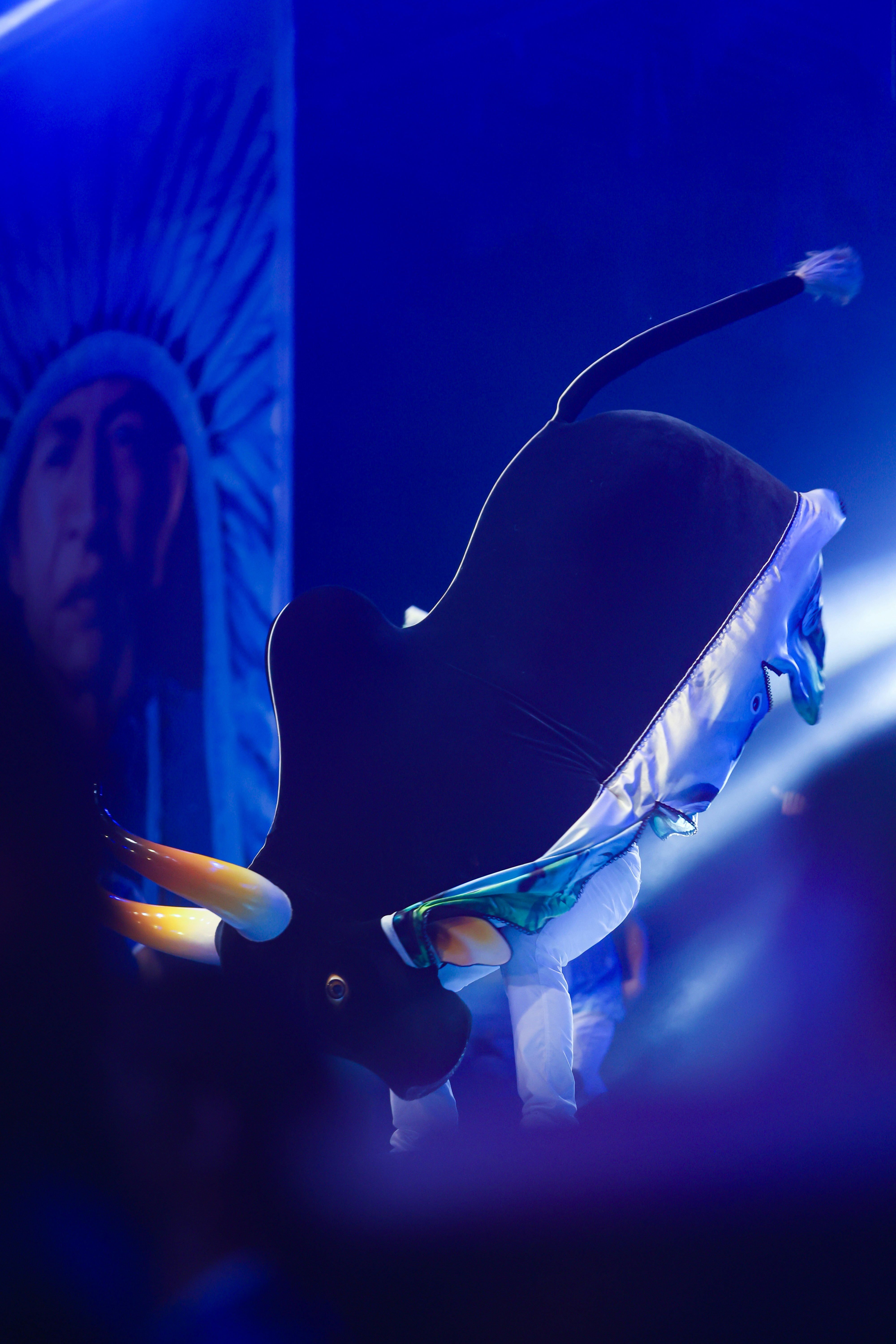 Uma fantasia de vaca flutua por um palco escuro.