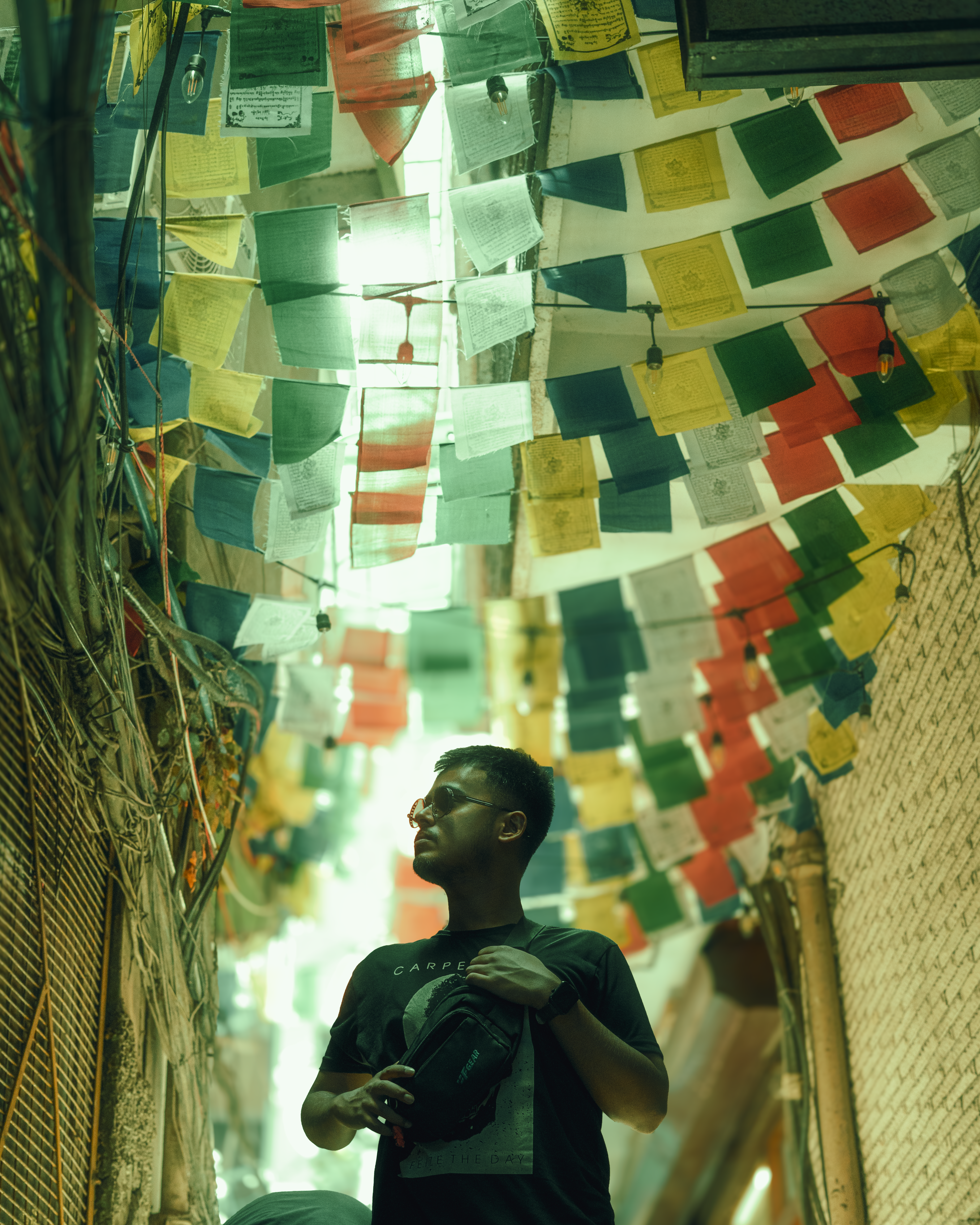 Man gazes up at prayer flags in an alley.