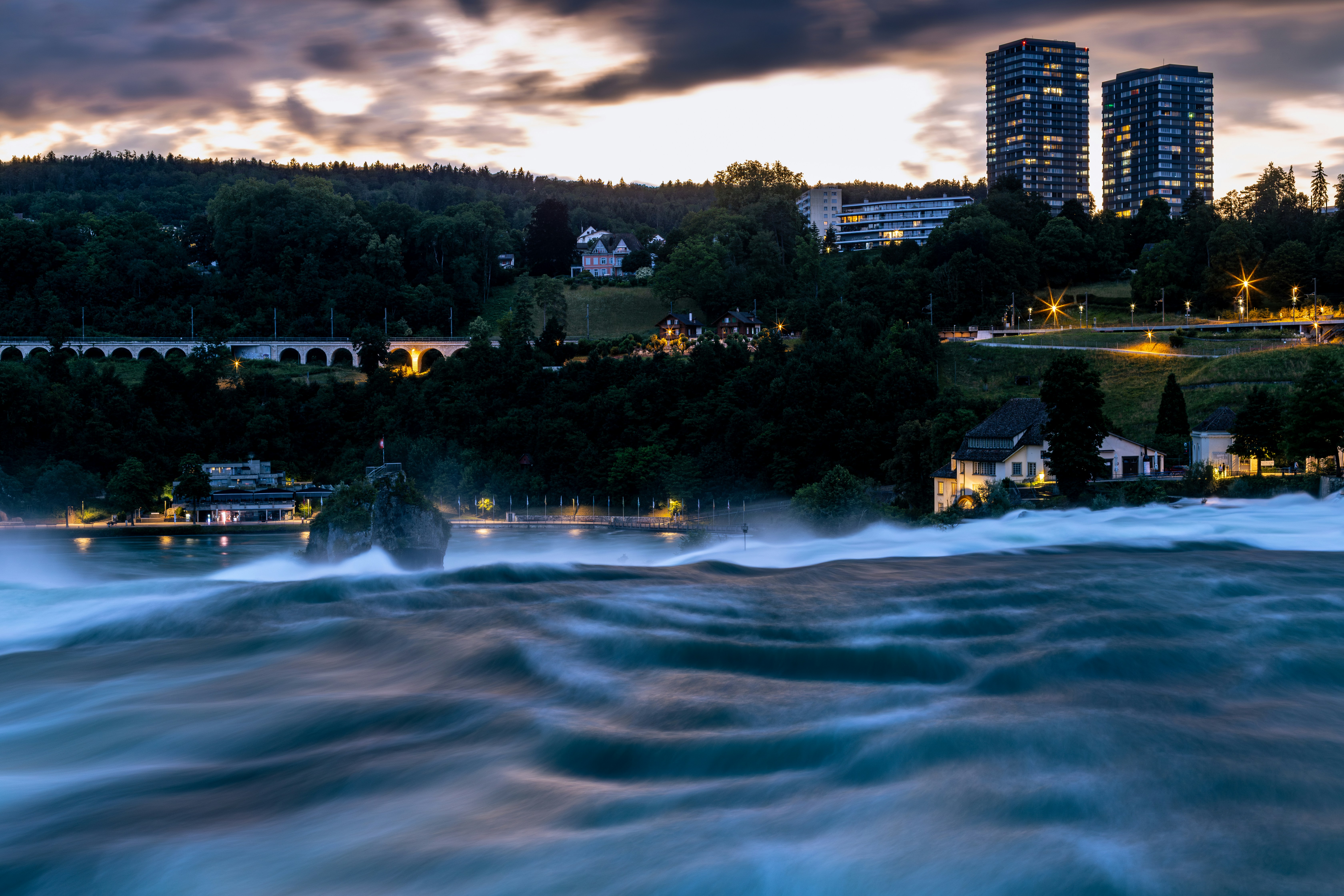 Rushing river with buildings in the distance.