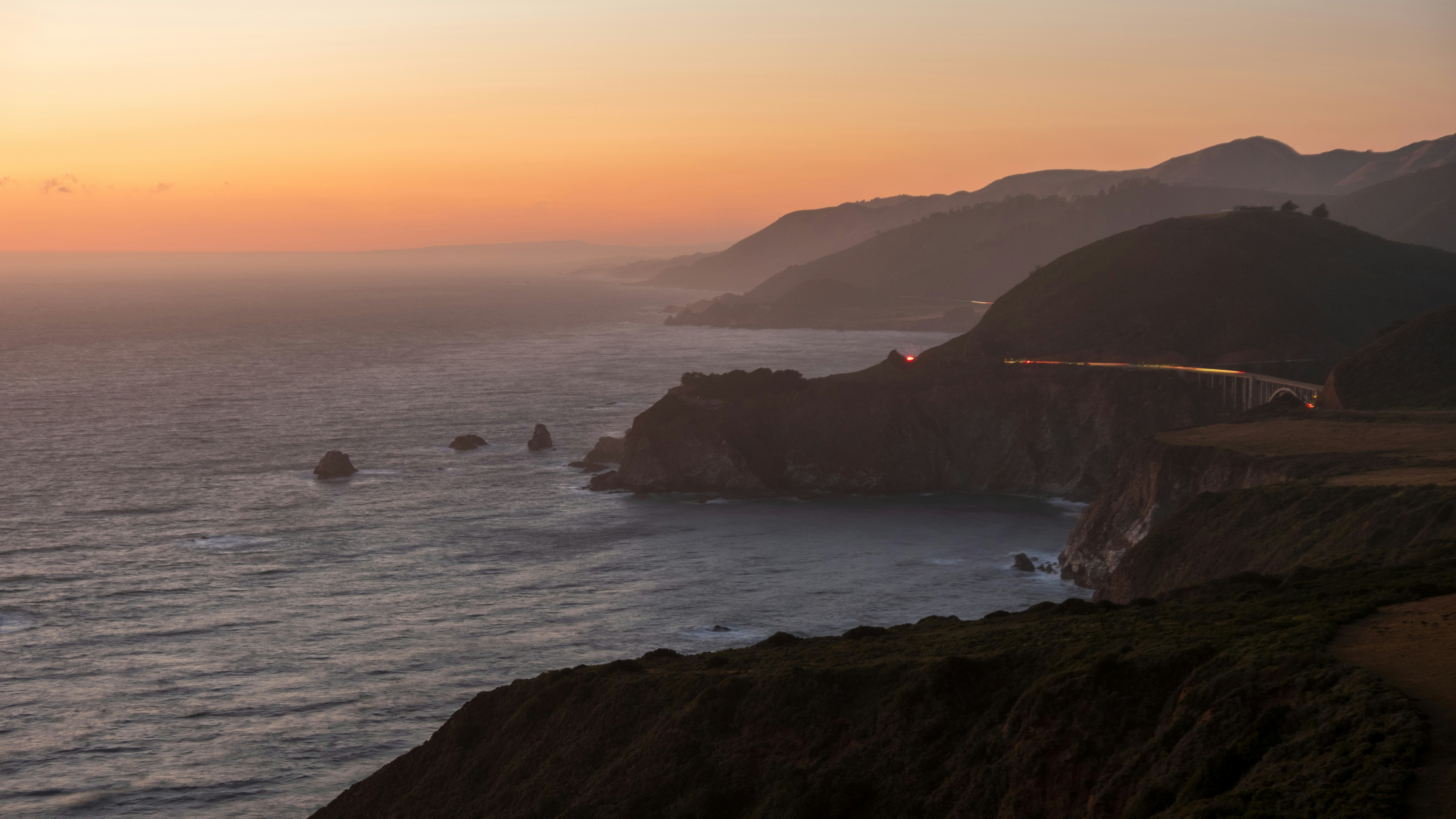 Sunset illuminates the coastline with mountains and sea.