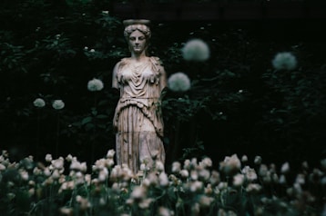 Ancient statue surrounded by flowers and foliage.
