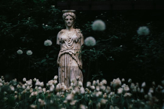 Ancient statue surrounded by flowers and foliage.