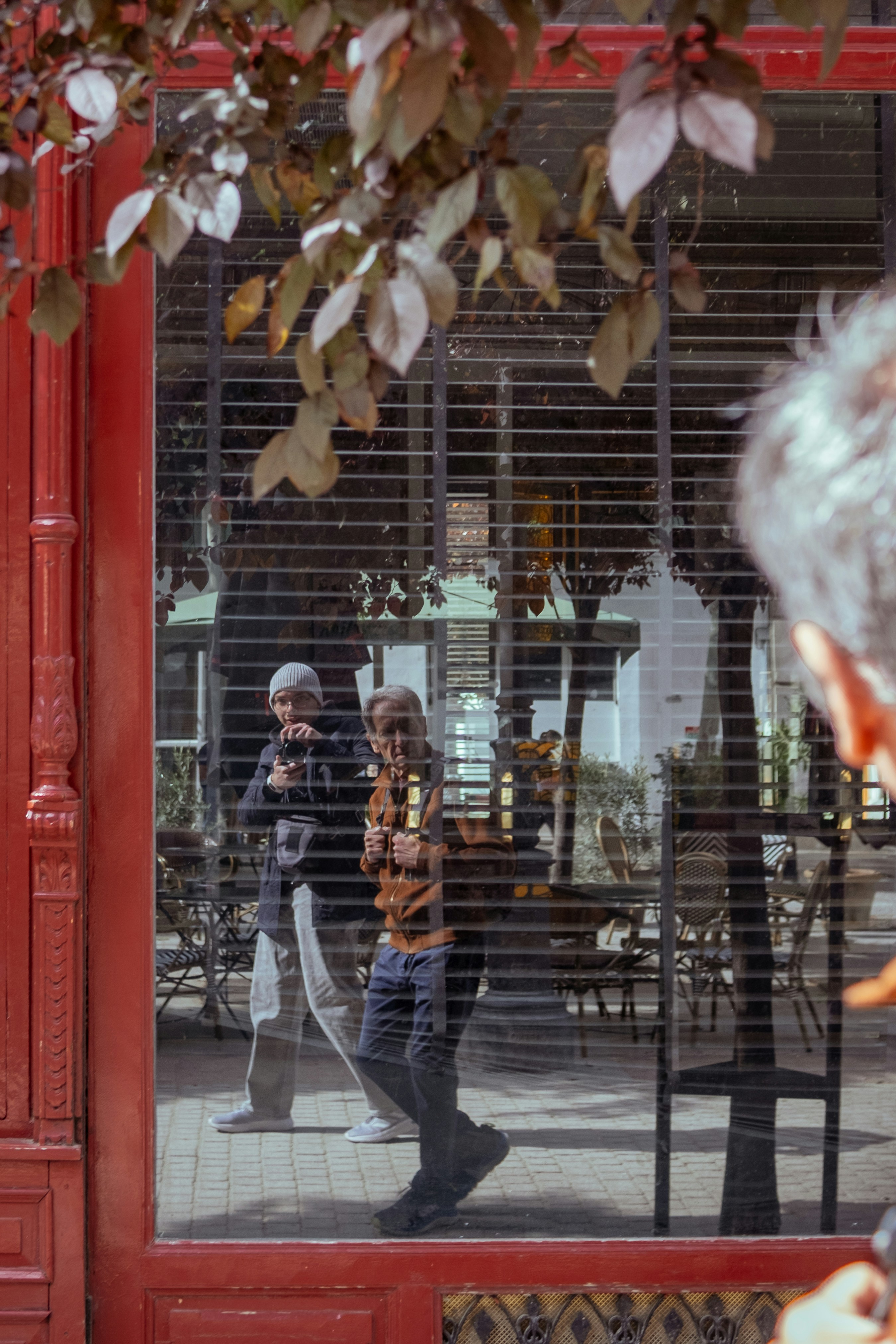 People are reflected in a window's closed shutters.