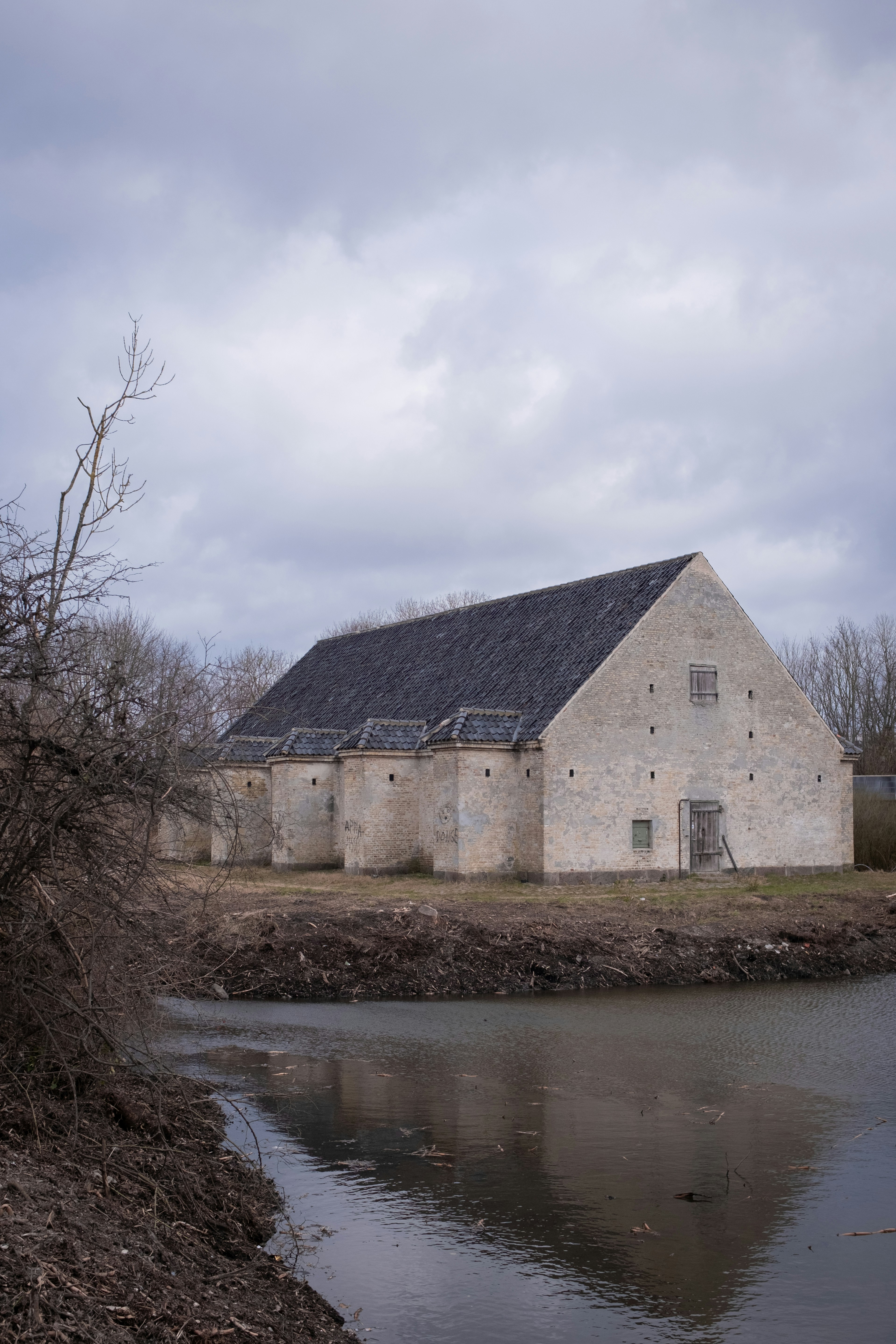 An old building stands beside water under cloudy skies.