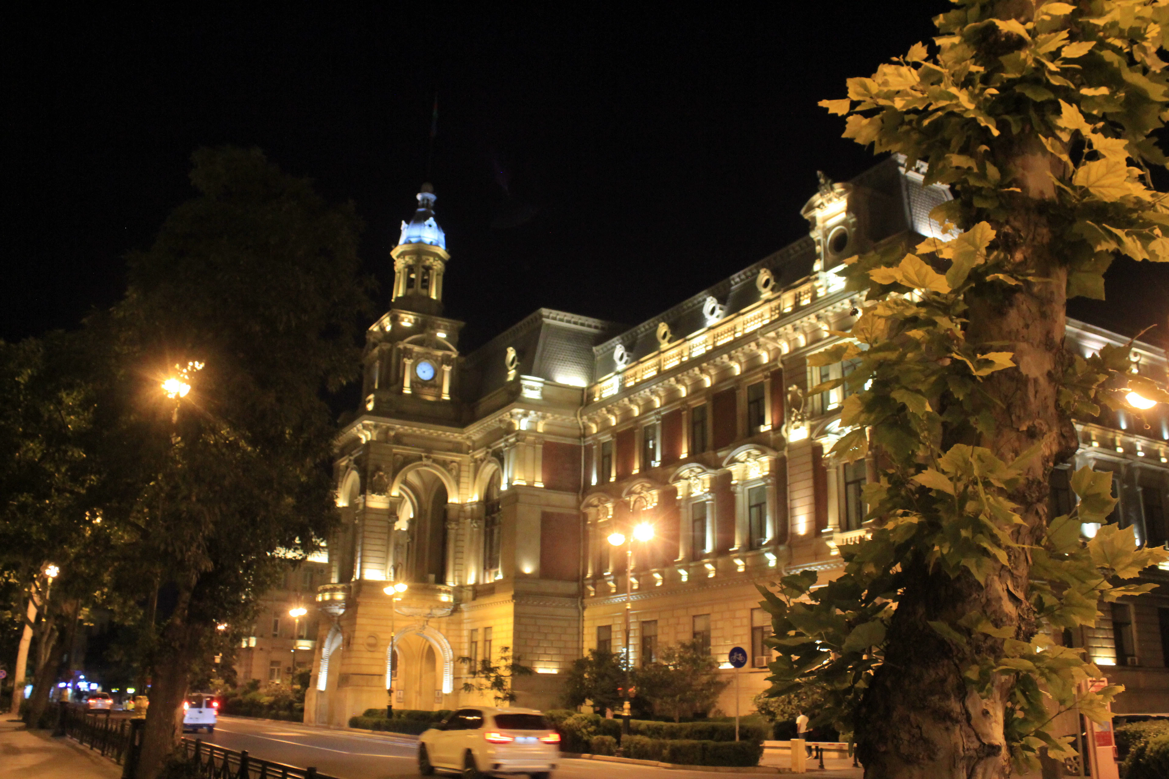 An ornate stone building glows under warm floodlights on a tree-lined Baku street at night.