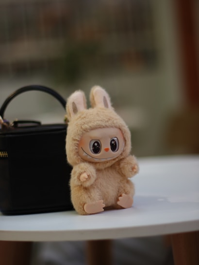 A plush bunny sits near a black handbag.