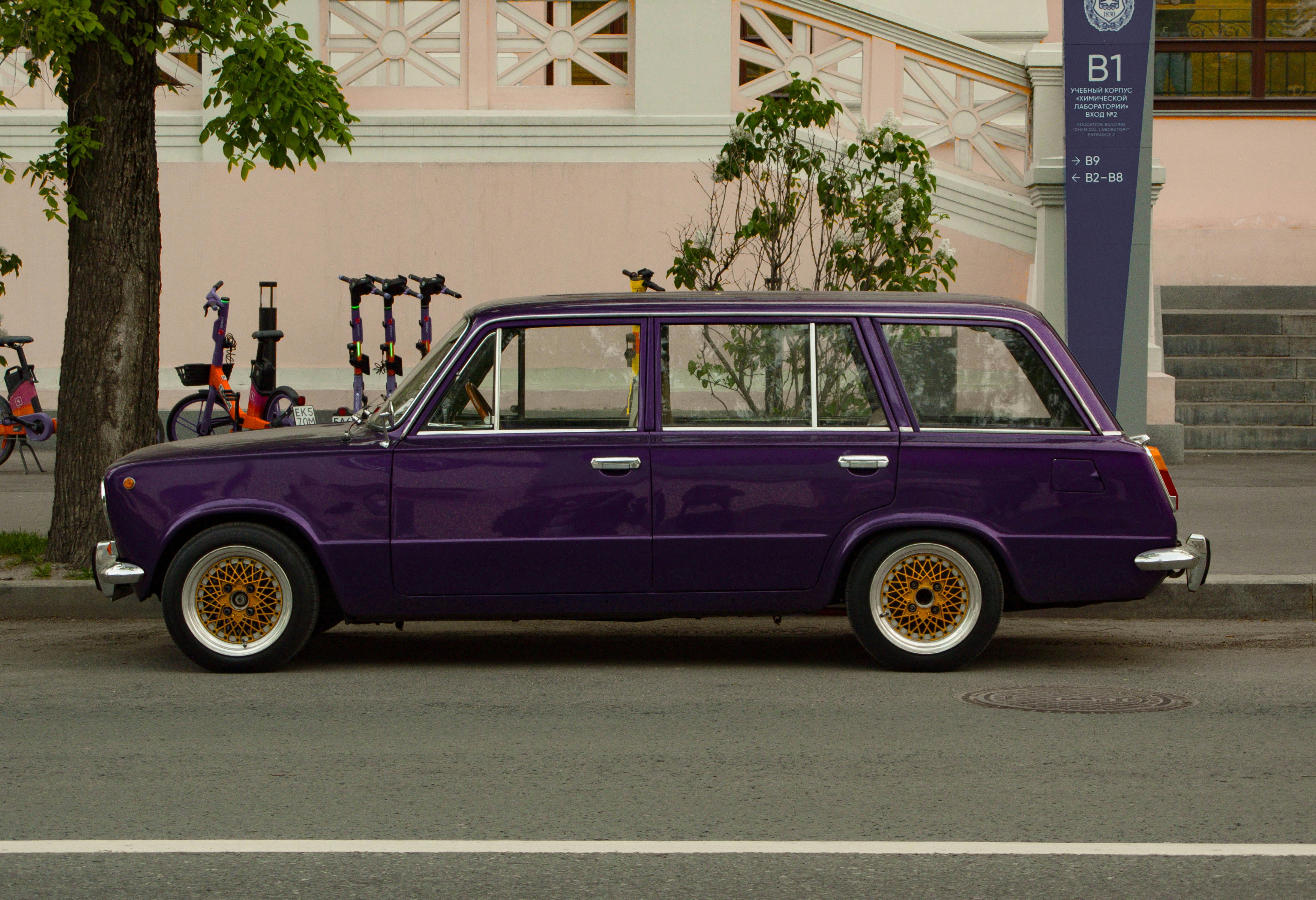 A purple station wagon parks by a sidewalk.