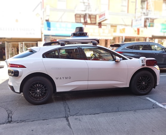 A white Waymo self-driving car with roof-mounted sensors moving through a city street