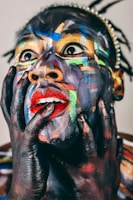 Face painted with vibrant colors, hands on cheeks.
