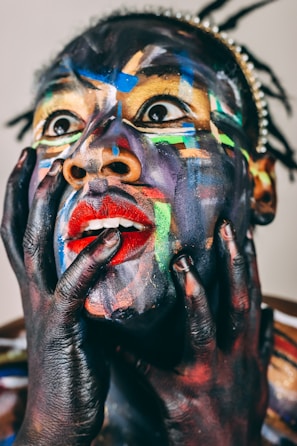 Face painted with vibrant colors, hands on cheeks.