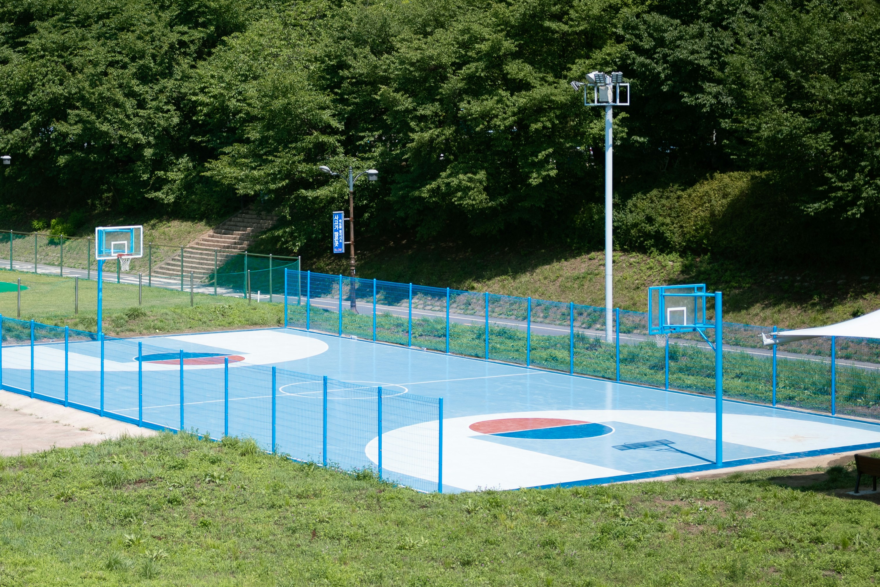 An outdoor basketball court is surrounded by greenery.