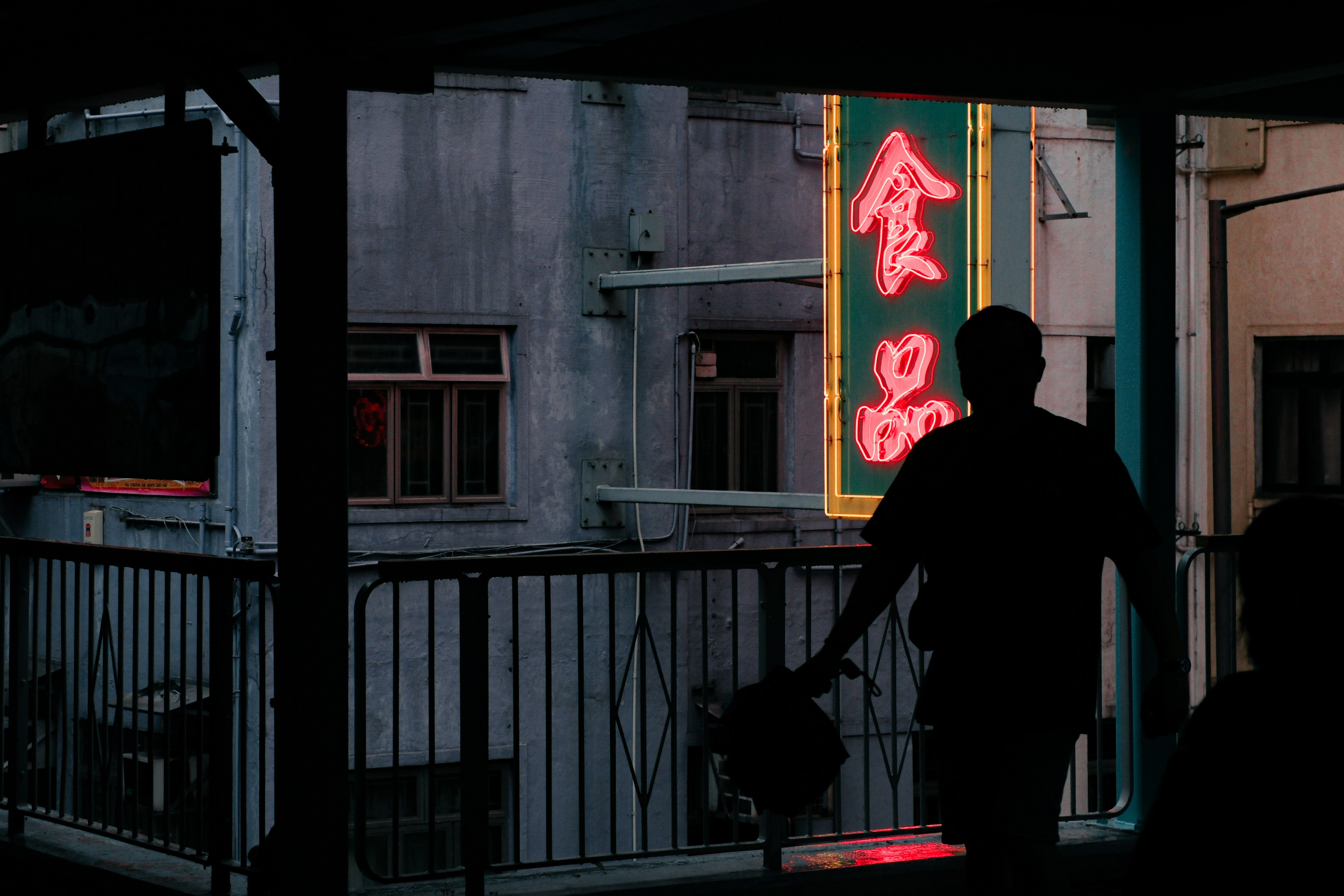 A silhouette of a person walks past a neon sign.