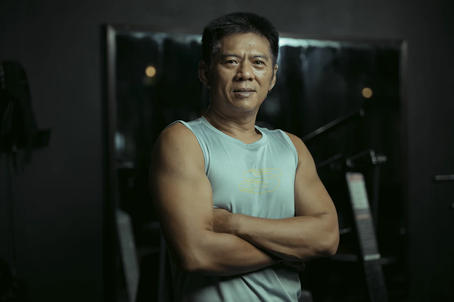 Fit adult man standing with arms crossed in a gym.