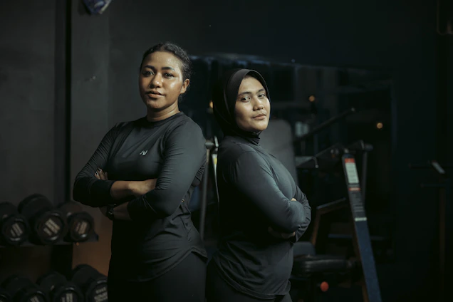 Two women stand confidently at a gym.