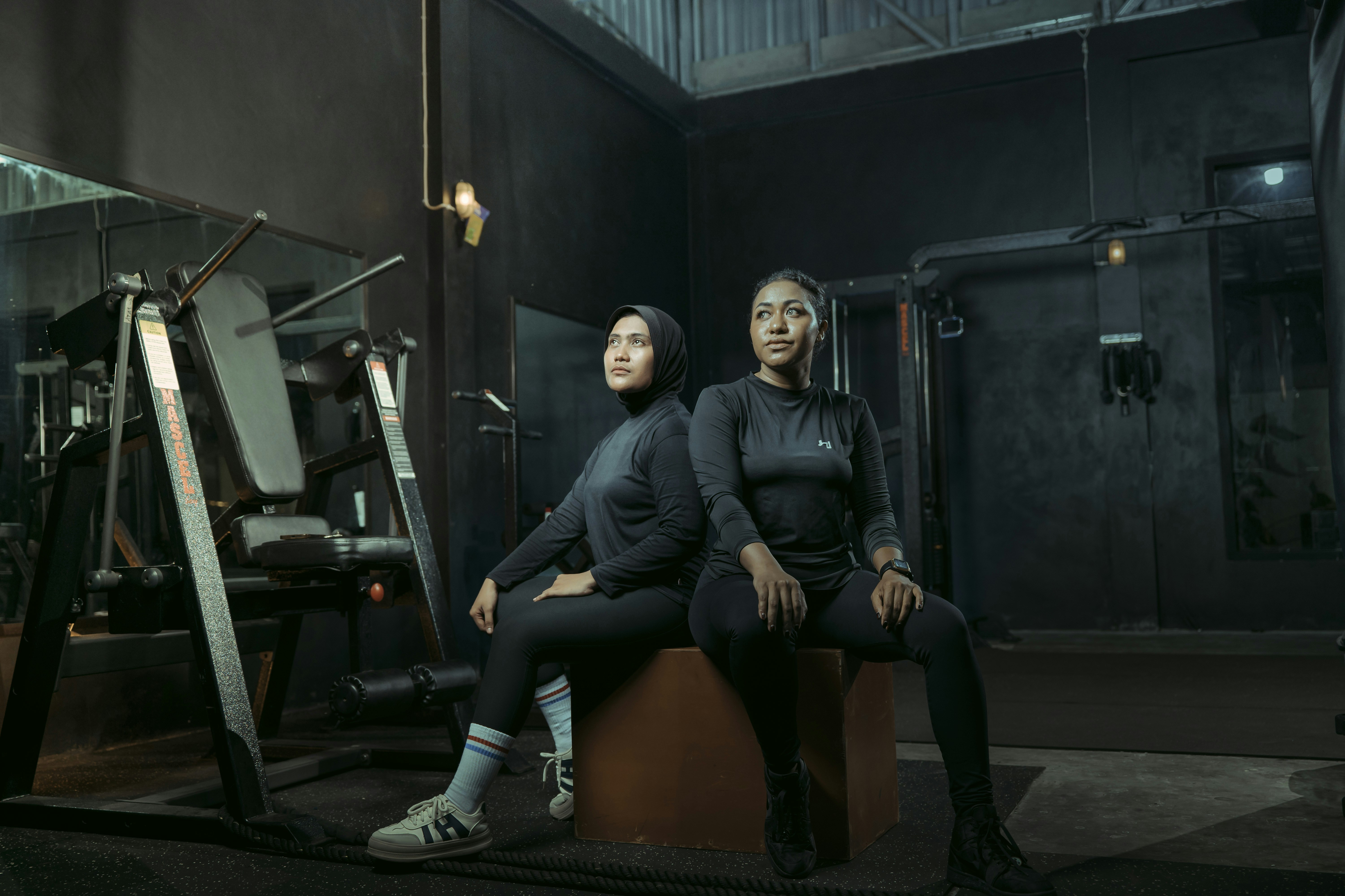 Two women pose in a dimly lit gym.