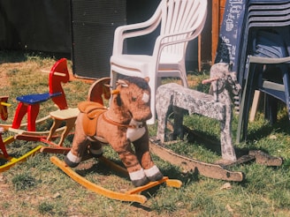 Many rocking horses are displayed outside on grass.