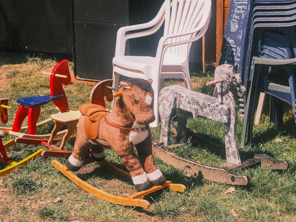 Many rocking horses are displayed outside on grass.