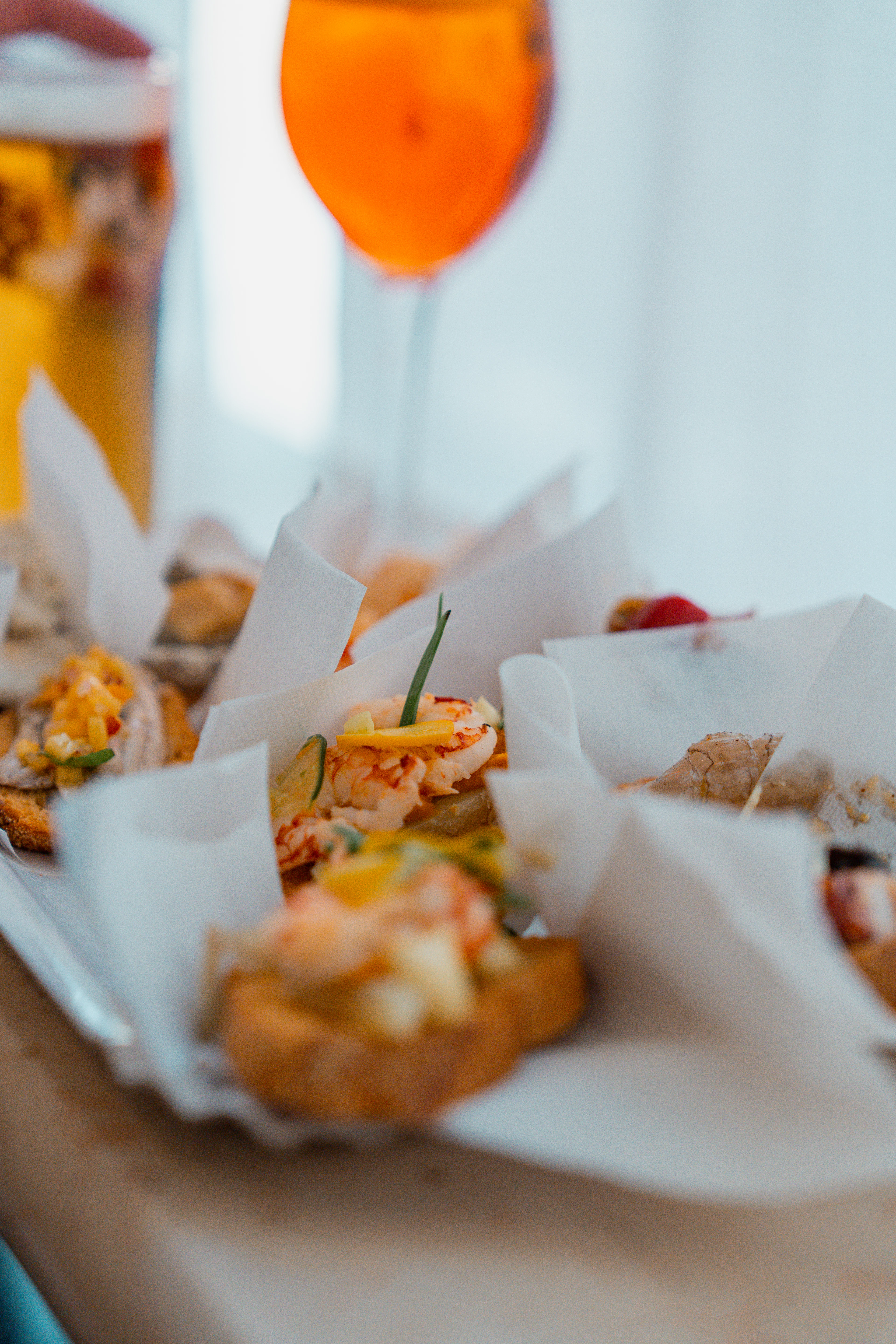 A tray of Venetian cicchetti topped with seafood beside a glass of bright orange spritz
