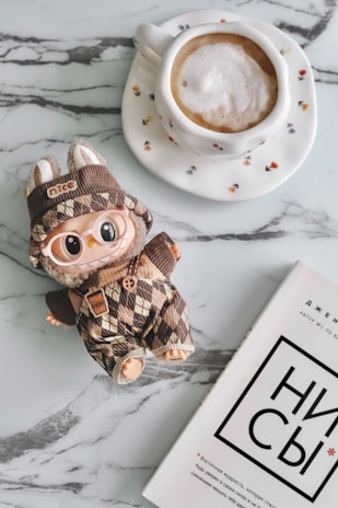 Coffee, a doll, and a book on a marble table.