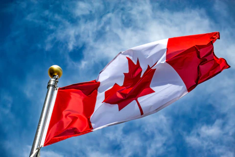 The canadian flag waves proudly against the sky.
