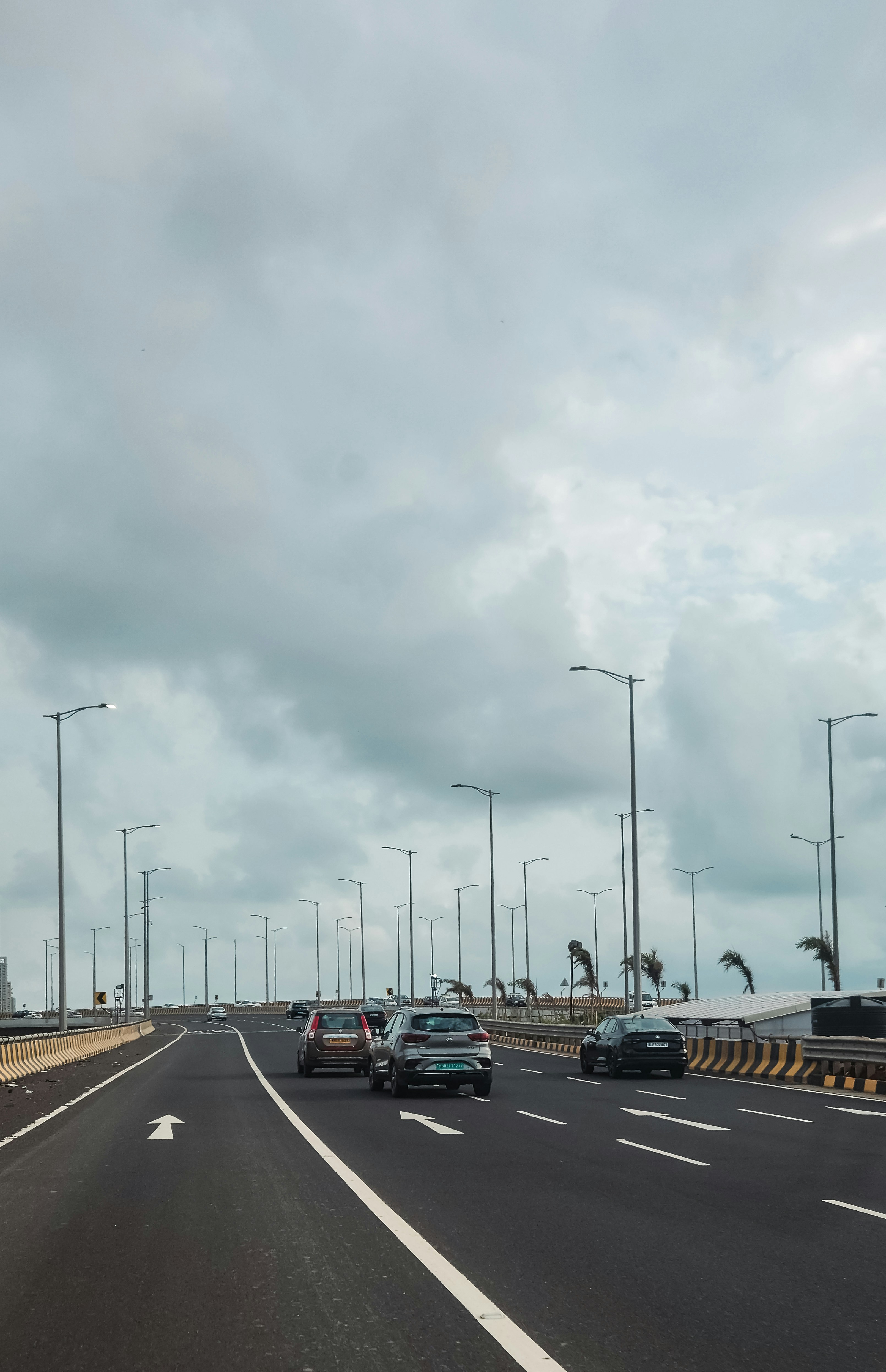 Cars drive on a highway under a cloudy sky.