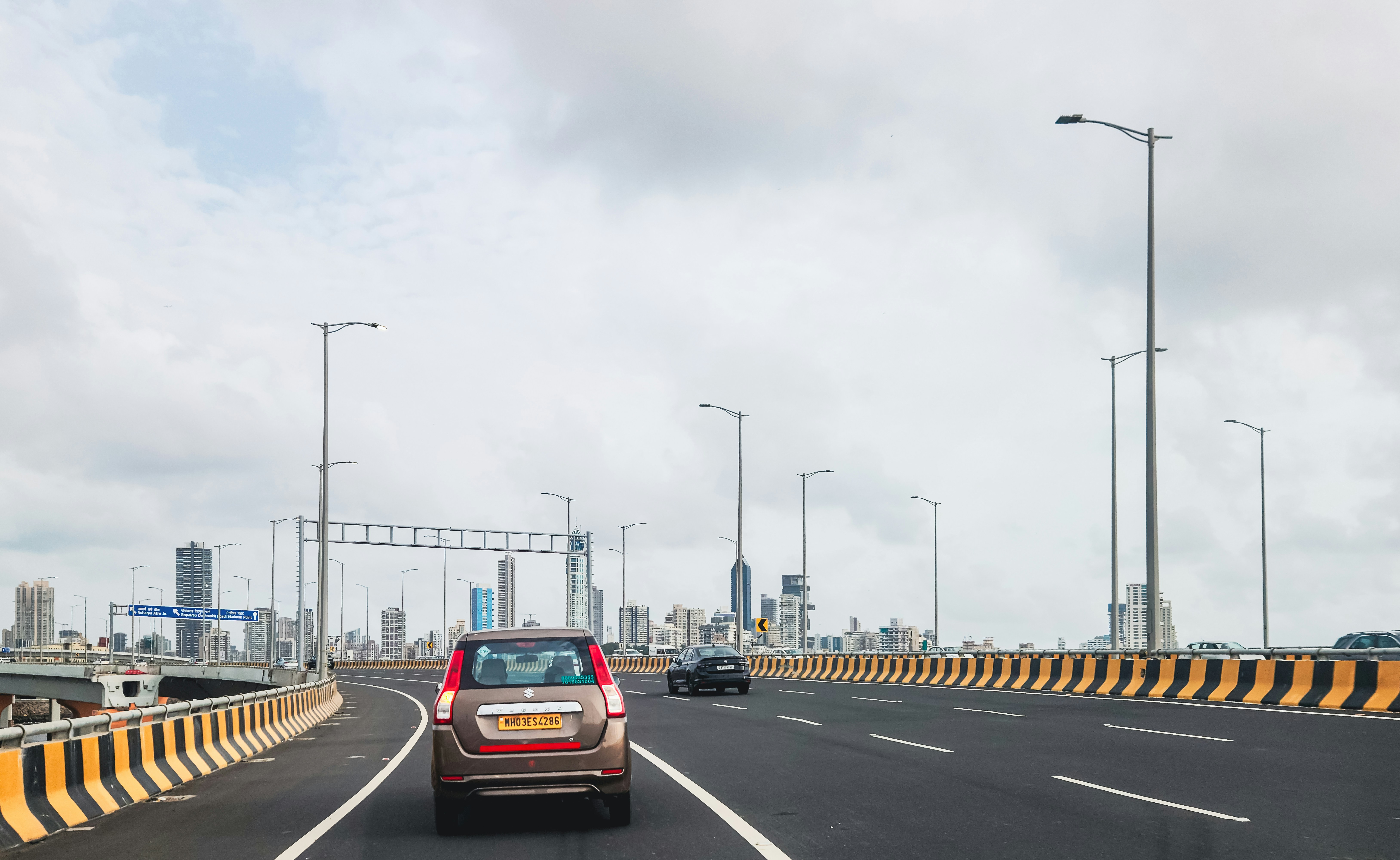 Cars drive on a road with a city skyline.
