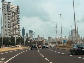 Cars drive on a city highway with tall buildings.
