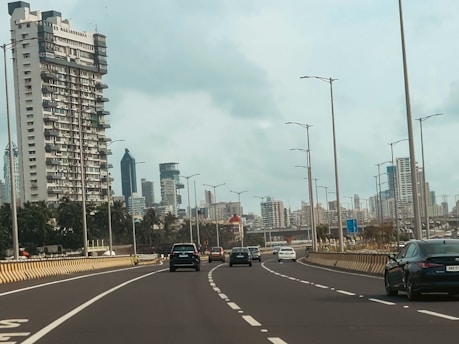Cars drive on a city highway with tall buildings.