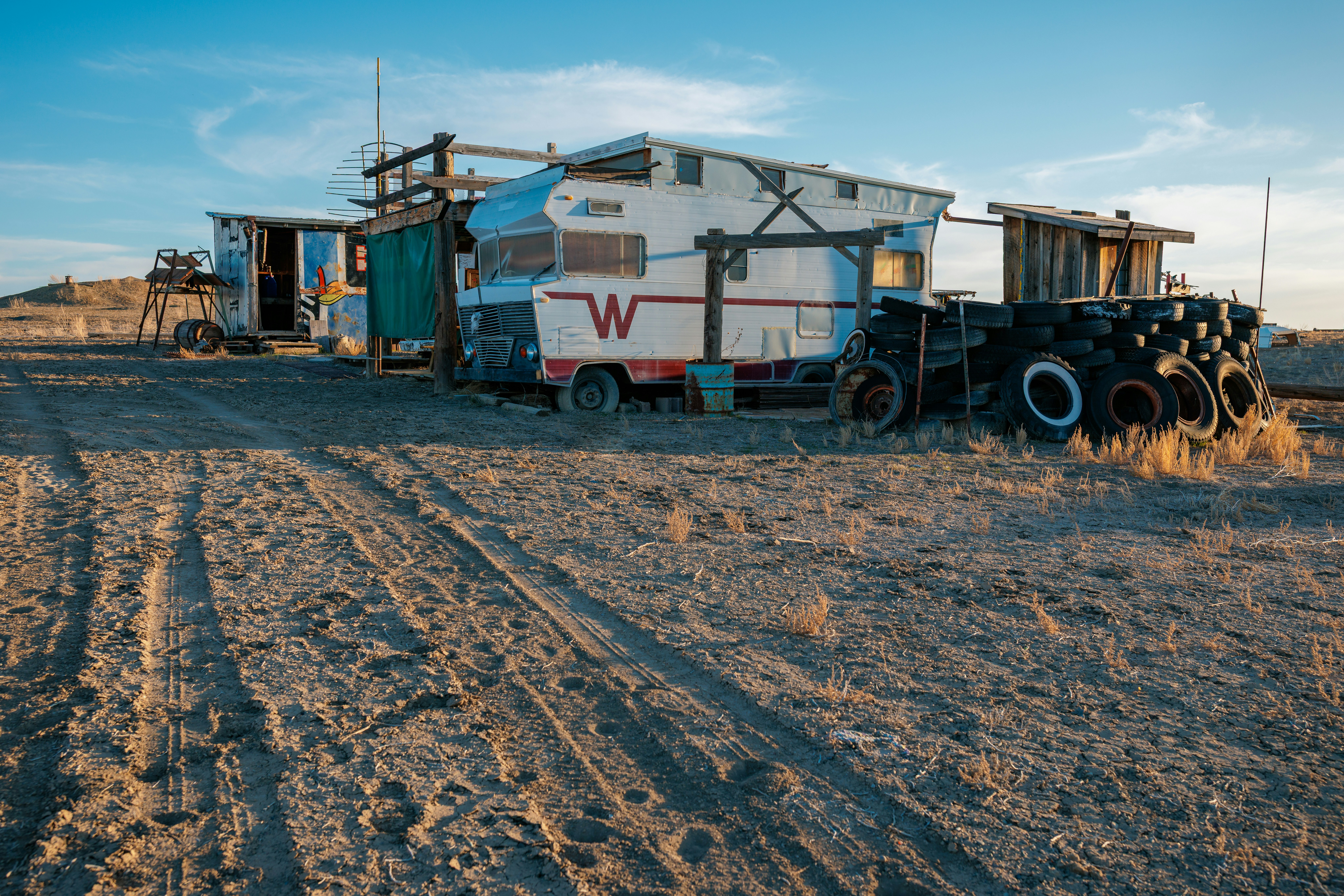 Abandoned rvs sit in a sunlit, dusty lot.